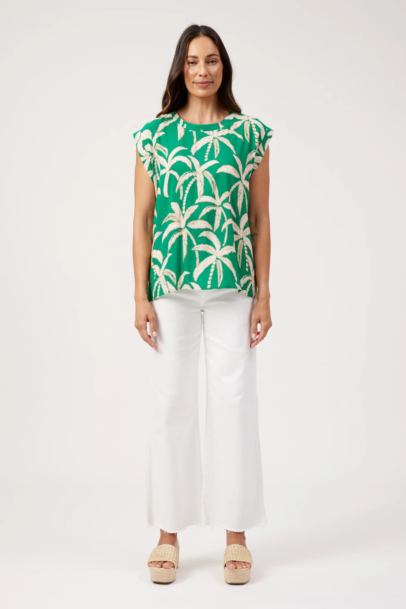 Image of Haven printed top, green palm tree print paired with white denim pants on a plain background 