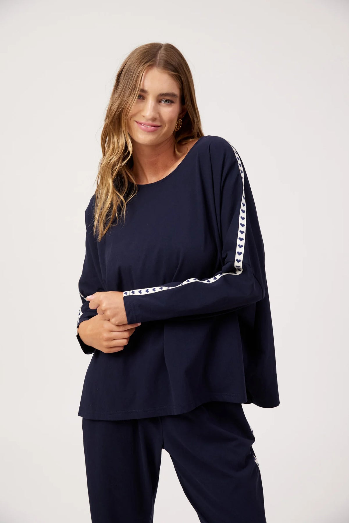 A woman modeling a Haven navy blue long-sleeve top with white patterned trim down the sleeves, paired with matching navy pants, against a plain light gray studio background.