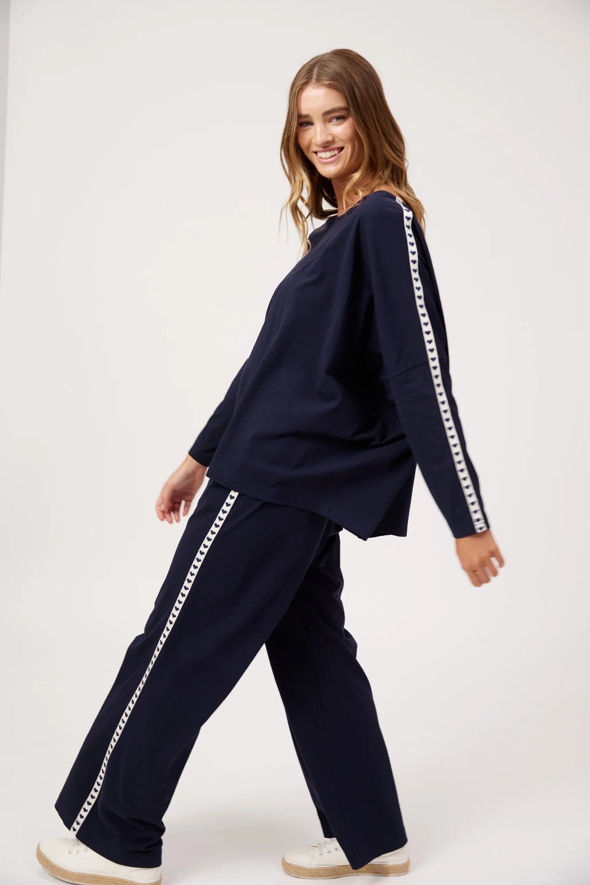 A woman modeling a Haven matching navy blue lounge set with white chain-link trim down the sleeves and pants, posed against a clean white studio background.
