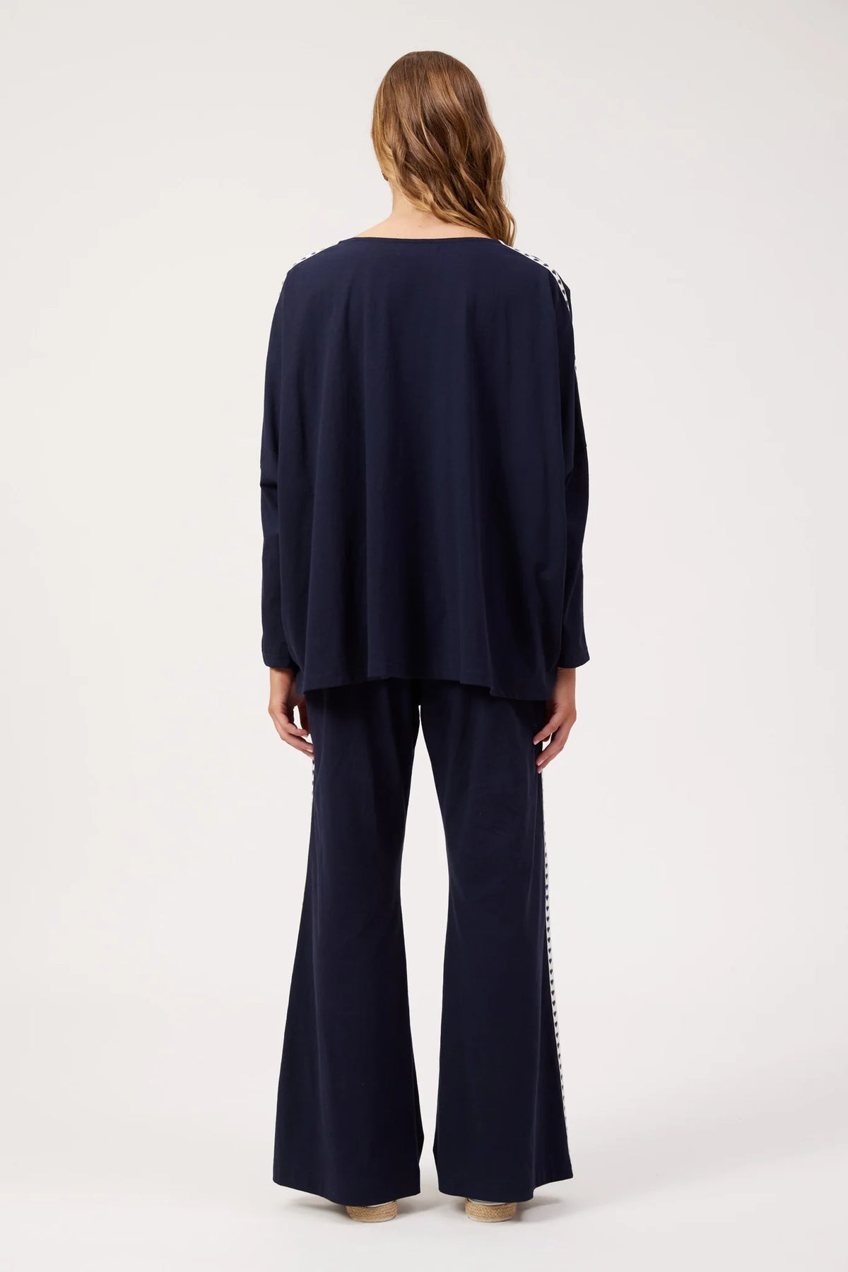 A woman viewed from the back wearing a Haven navy blue two-piece outfit consisting of a loose long-sleeve top and matching wide-leg pants with decorative silver chain detailing along the outer seams.