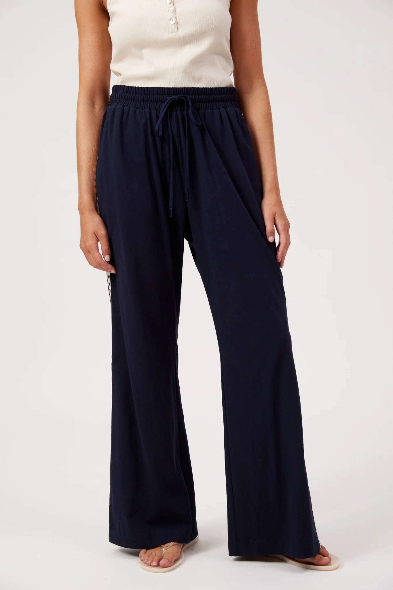 Image of A model wearing Haven navy blue wide-leg drawstring pants with a cream sleeveless top, standing against a light gray studio background.