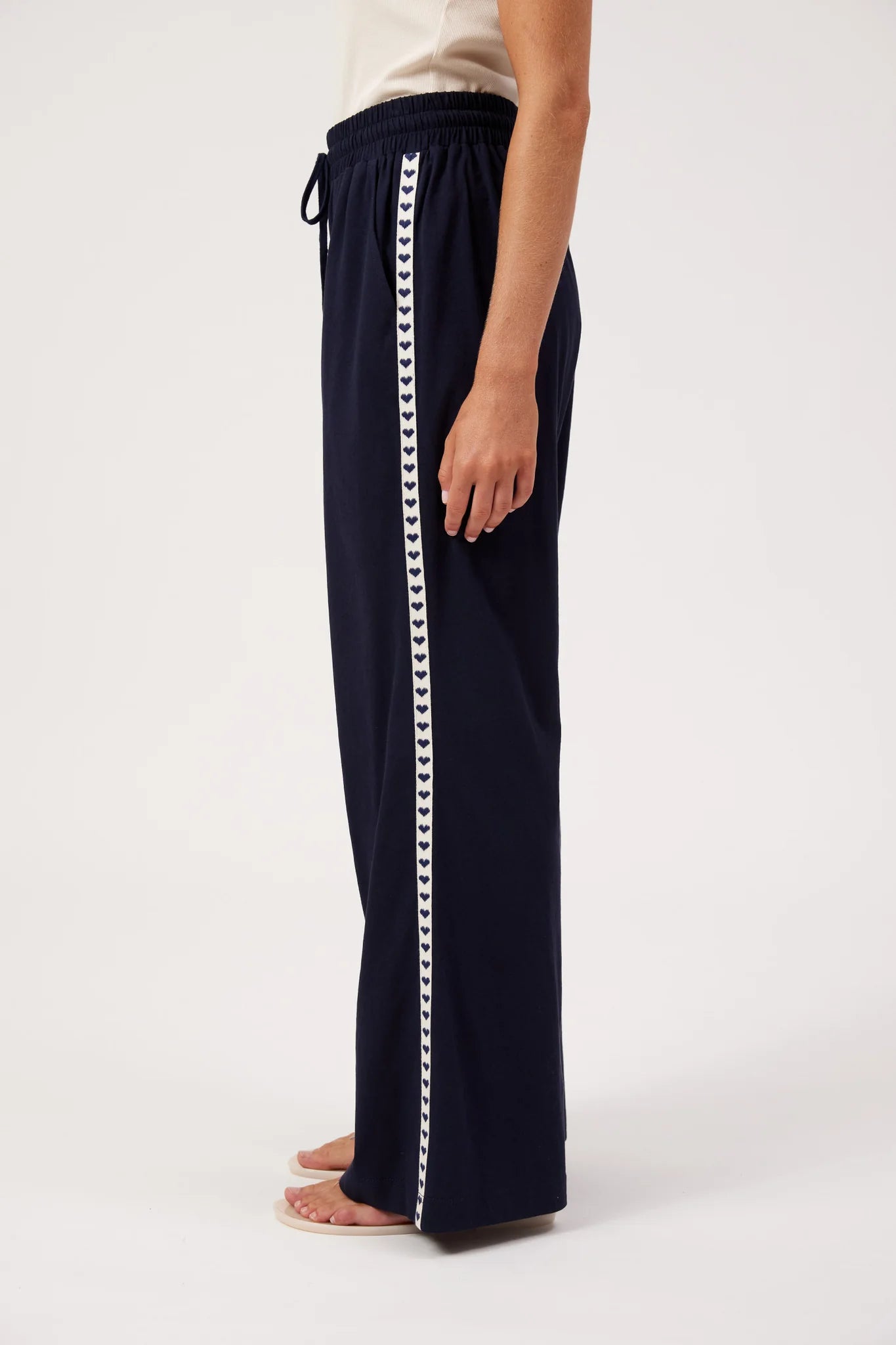 Image of A woman shown from the side wearing Haven navy wide-leg pants with a white sleeveless top, standing against a plain white studio background.