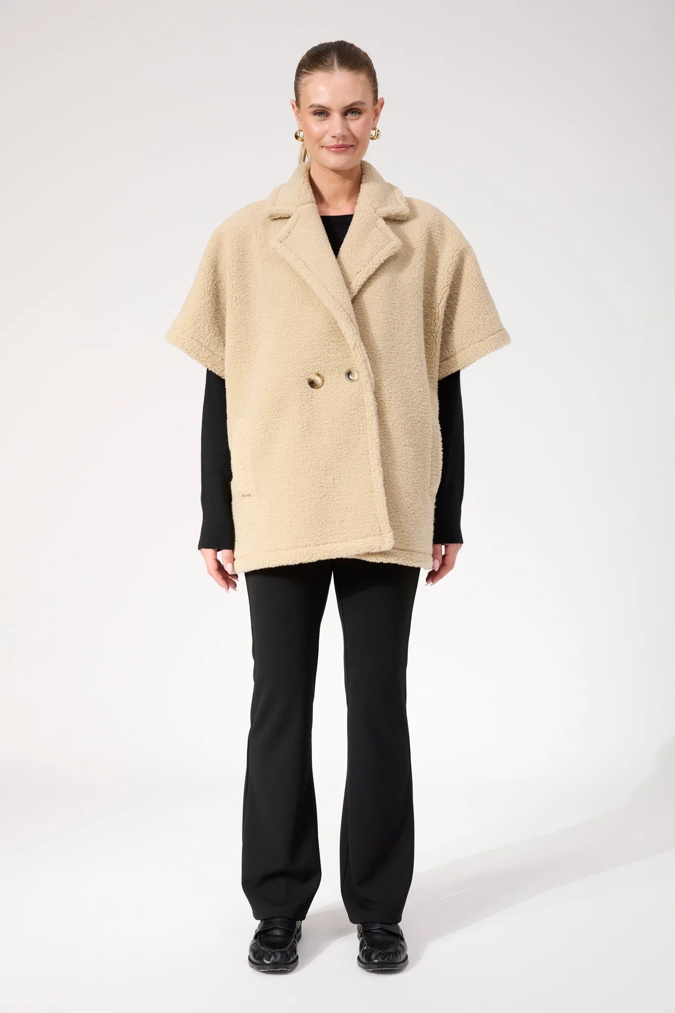 Image of Woman wearing Haven oversized vest in a natural colour paired with black pants on a plain background 