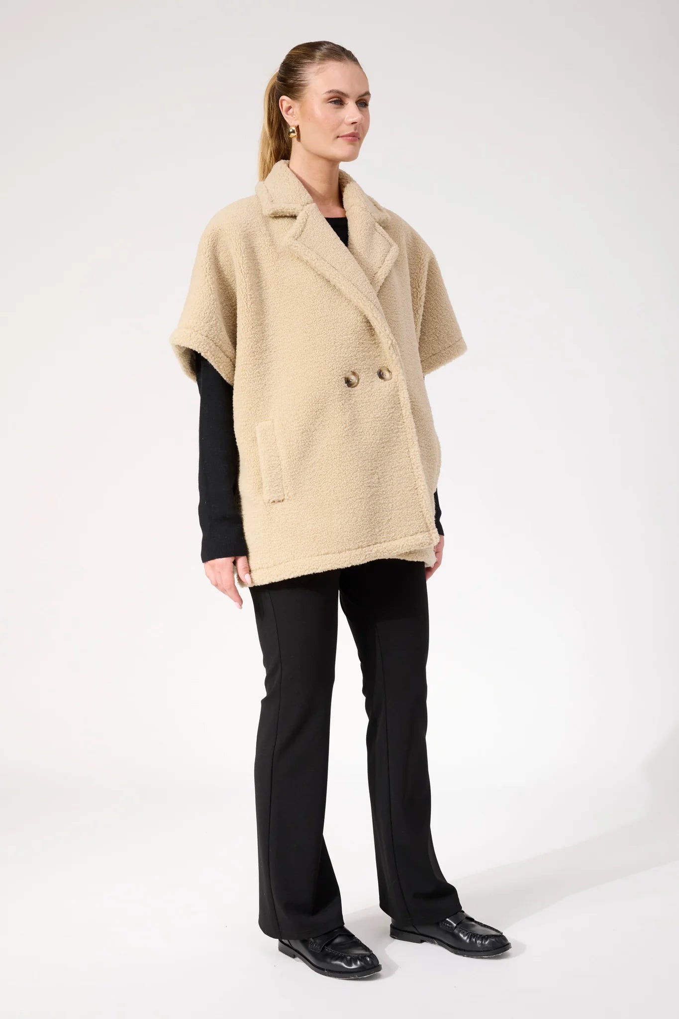 Image of Woman wearing Haven oversized vest in a natural colour paired with black pants on a plain background 
