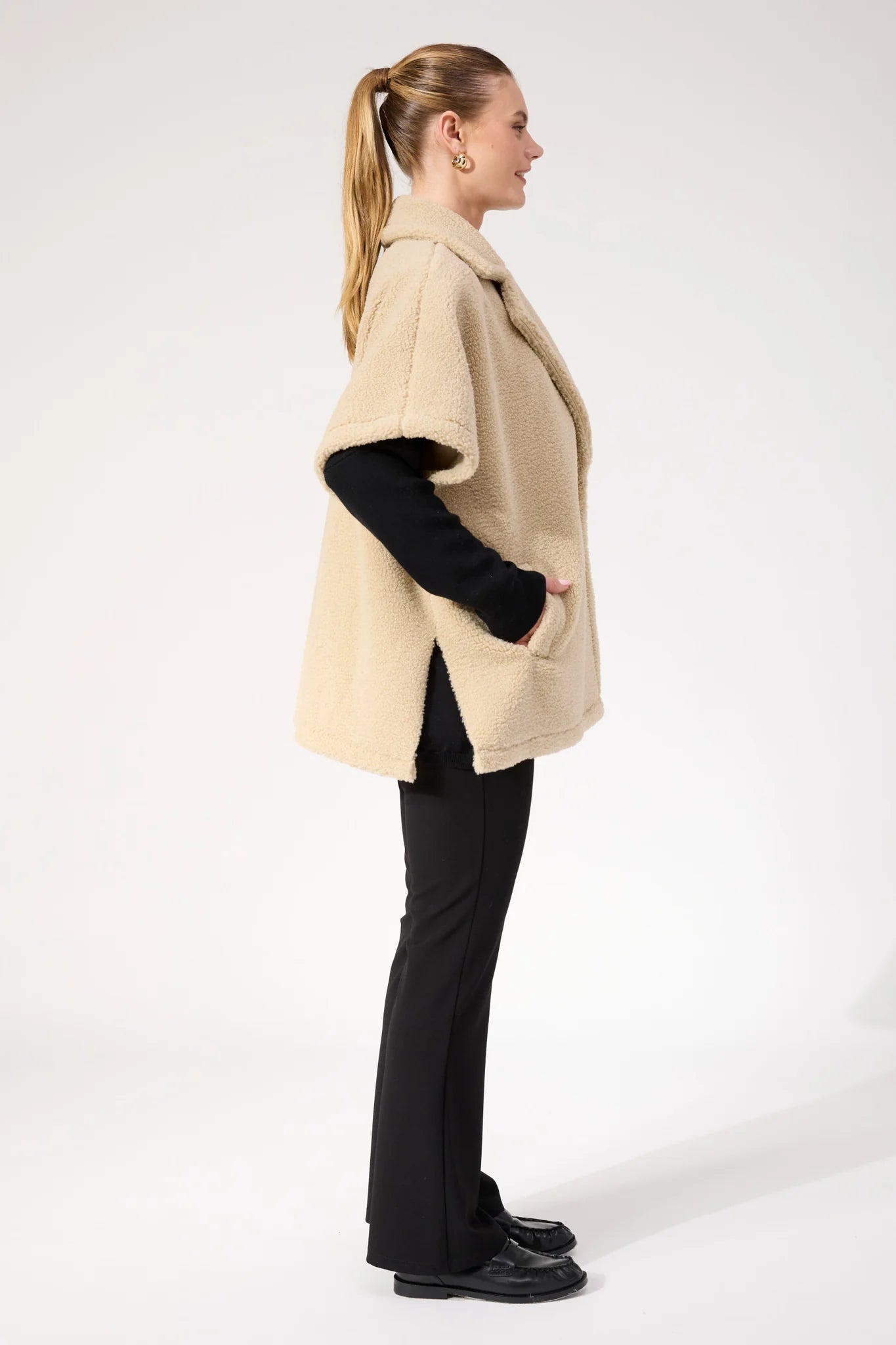 Image of Woman wearing Haven oversized vest in a natural colour paired with black pants on a plain background 