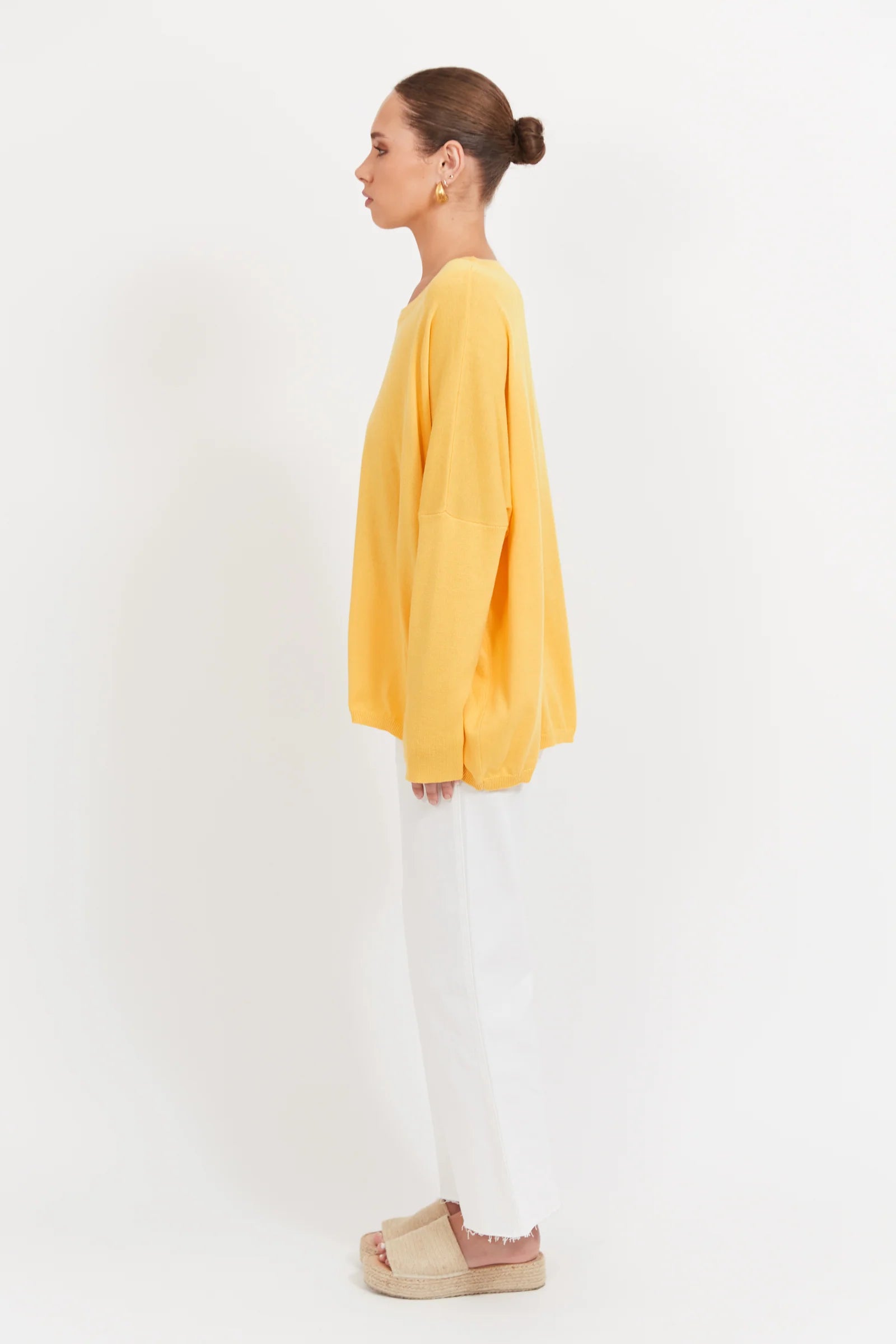 Woman wearing a Banana coloured knit paired with white denim jeans on a plain background