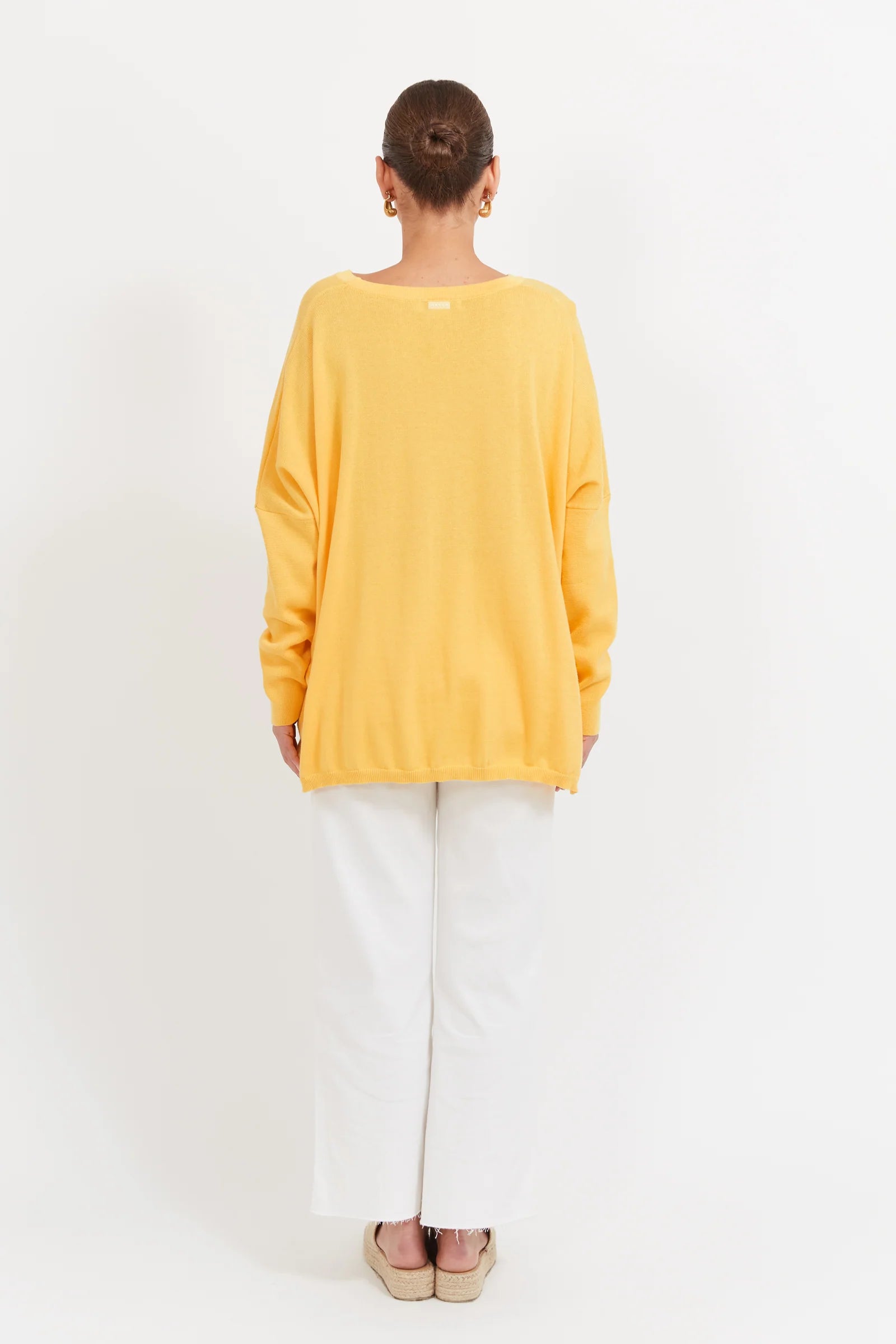Image of Woman wearing a Banana coloured knit paired with white denim jeans on a plain background