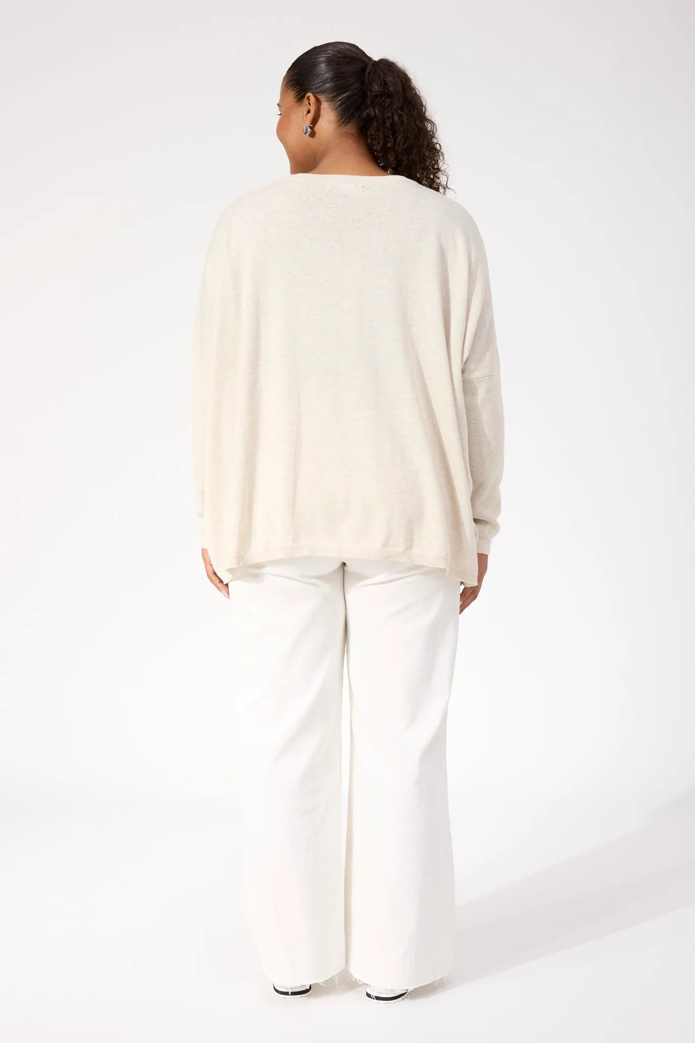 Image of Woman wearing Haven Knit paired with white denim jeans on a plain background