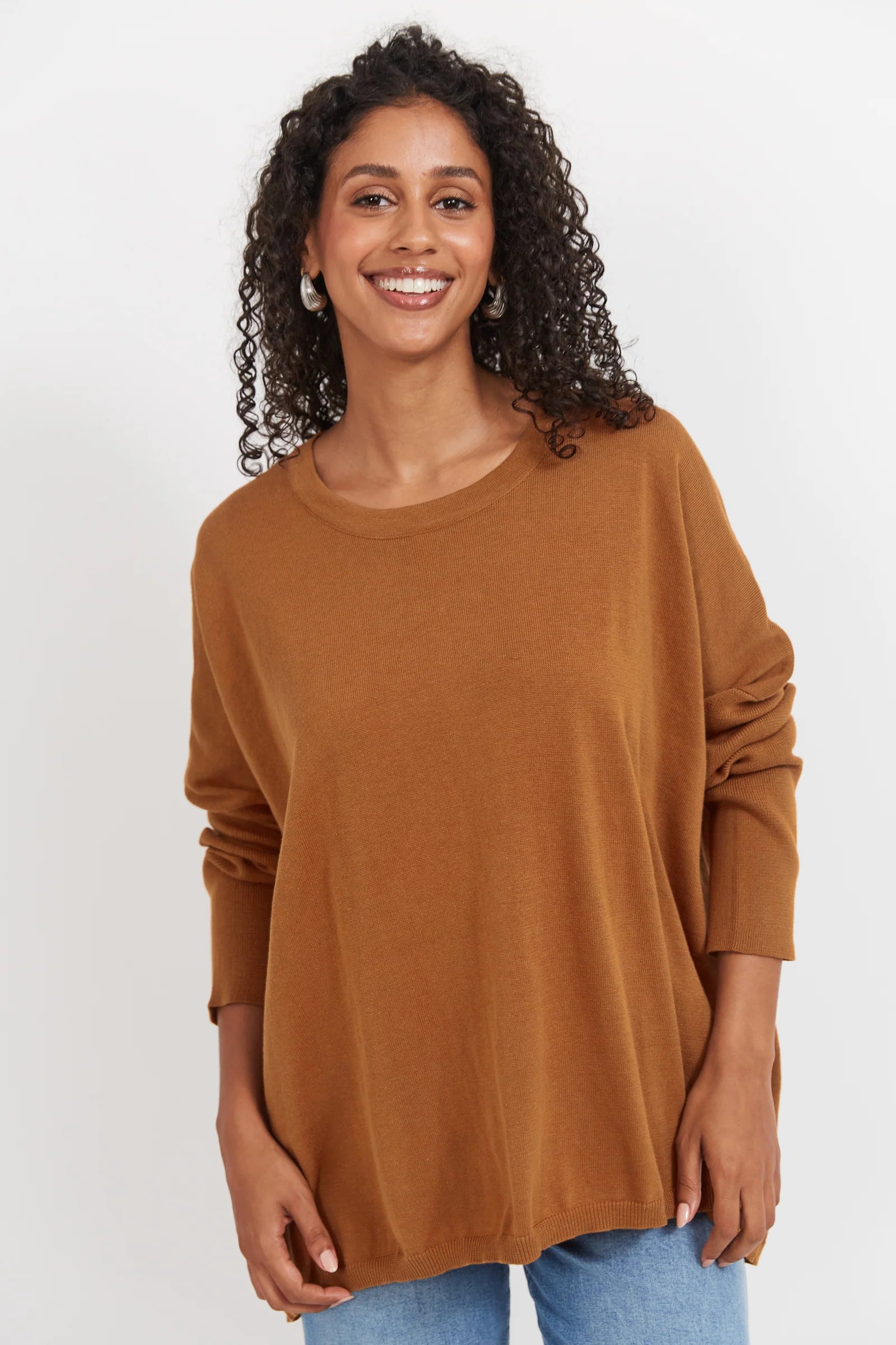 Image of Woman wearing tan Haven knit paired with denim jeans on a plain background