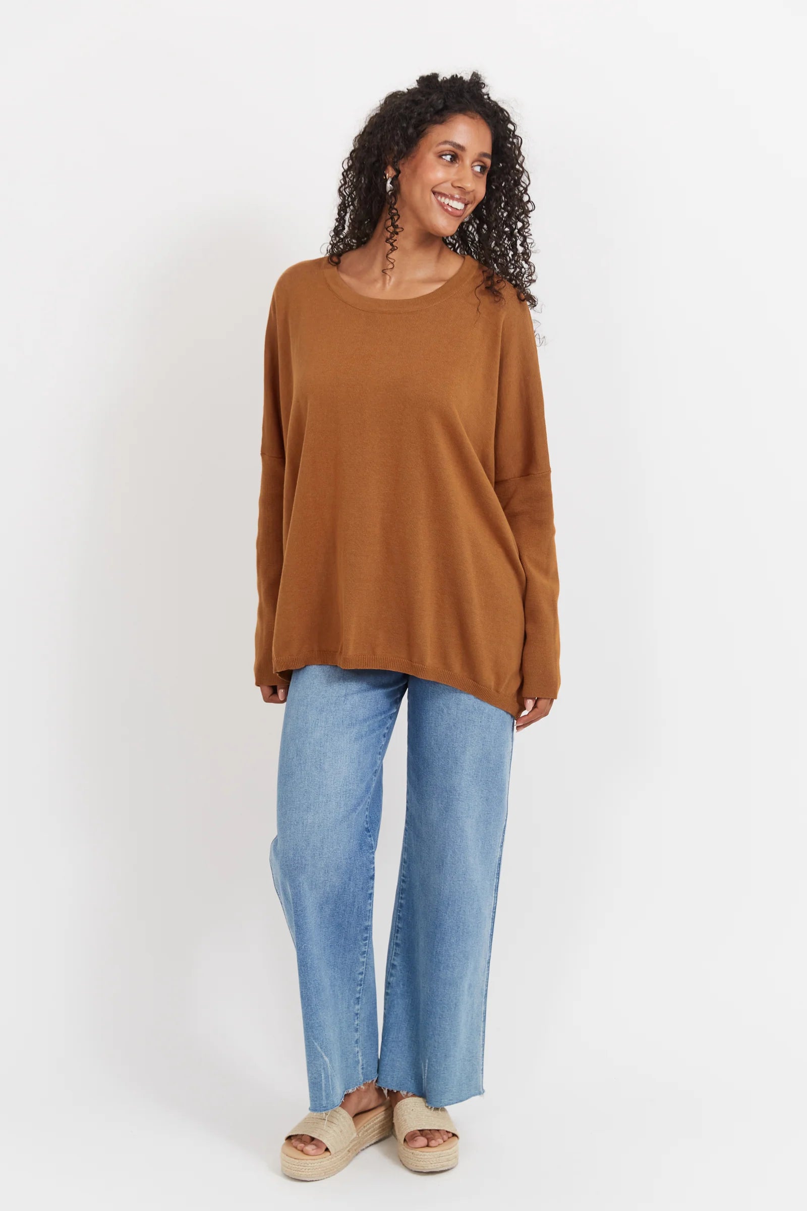 Woman wearing tan Haven knit paired with denim jeans on a plain background