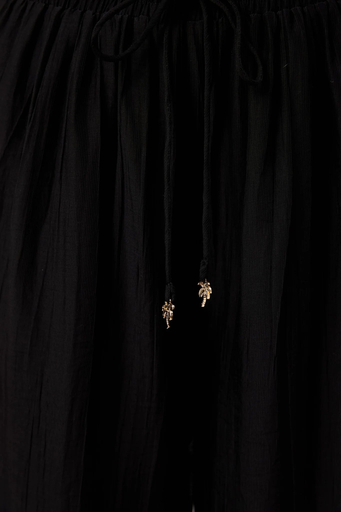 Image of Close-up of Haven black drawstring pants with small gold palm tree charms hanging from the drawstrings.