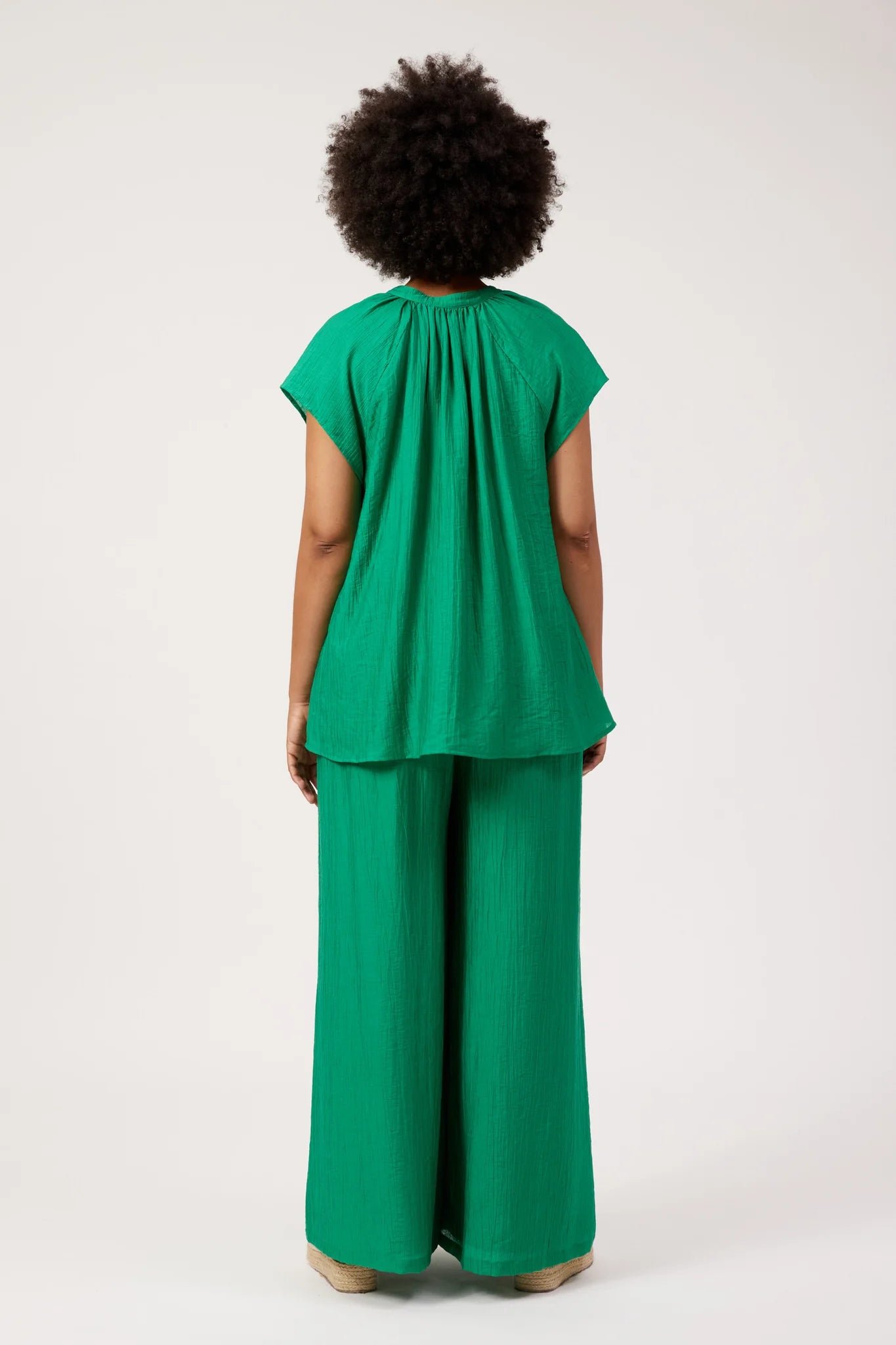 Image of A woman viewed from the back wearing a Haven bright green matching set consisting of a short-sleeve top with a gathered neckline and wide-leg pants, against a plain light background.