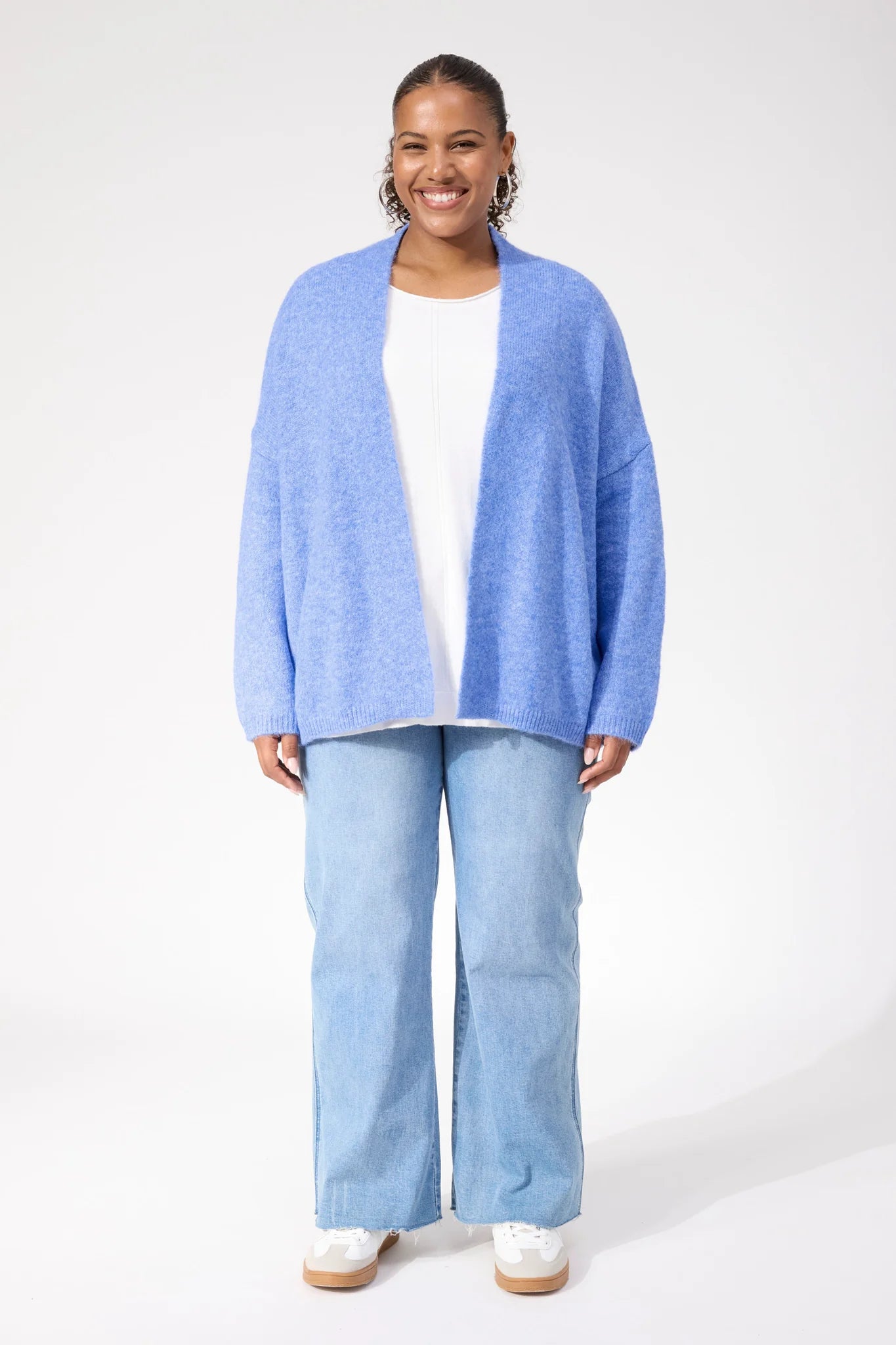 Image of Woman wearing Haven blue cardigan paired with denim jeans on a plain background