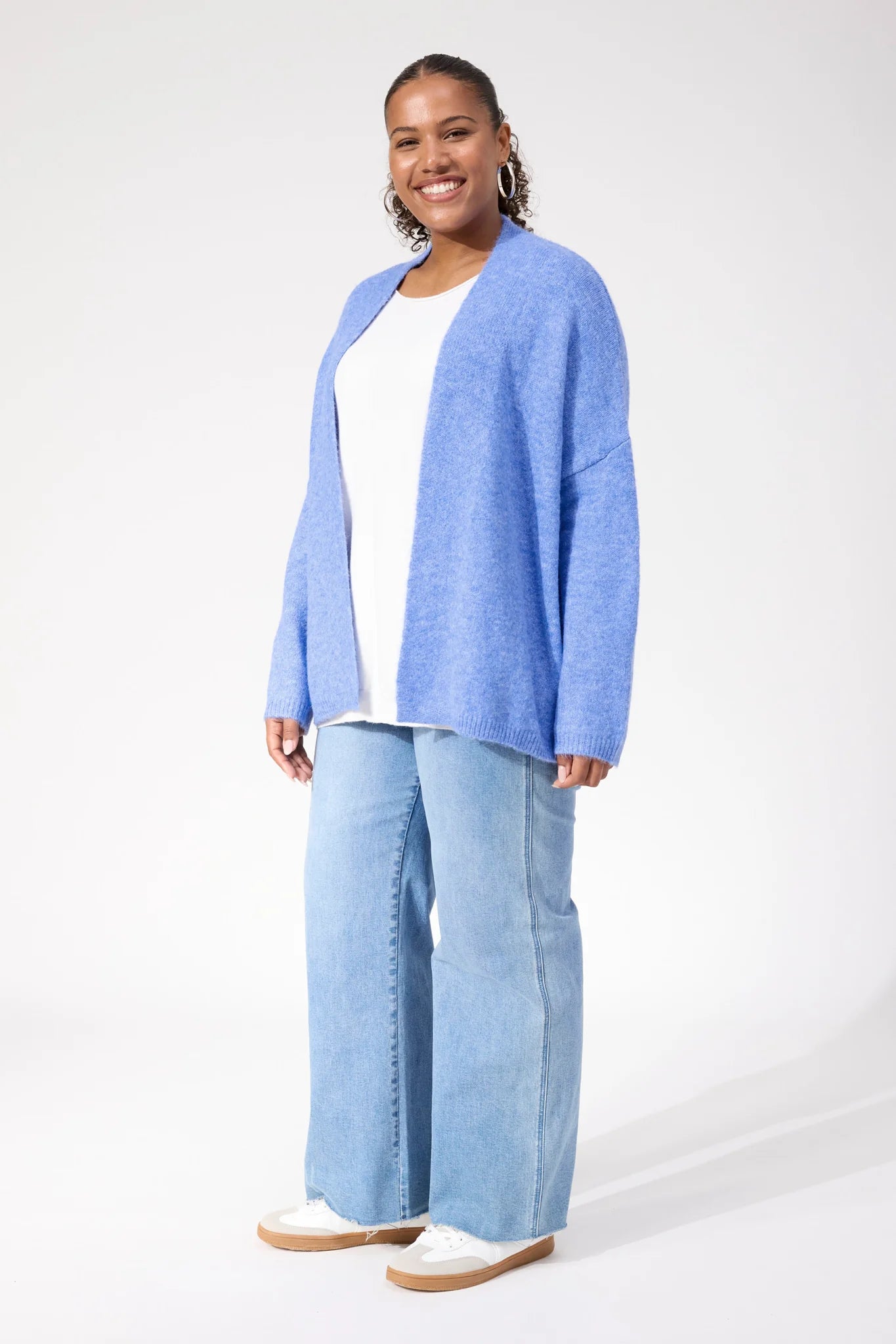 Image of Woman wearing Haven blue cardigan paired with denim jeans on a plain background