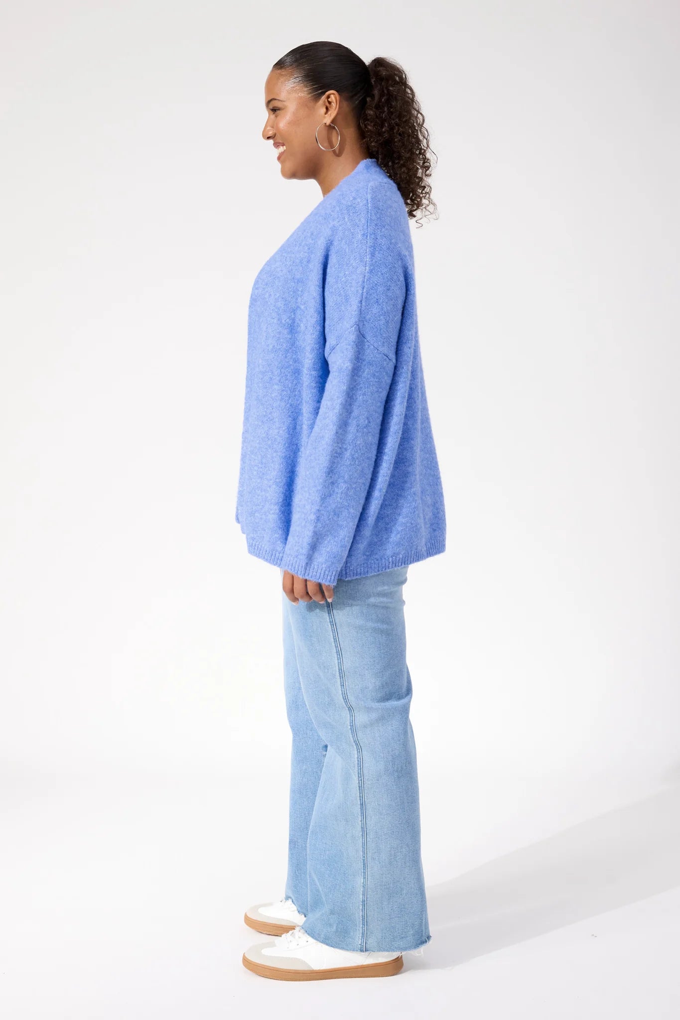 Image of Woman wearing Haven blue cardigan paired with denim jeans on a plain background
