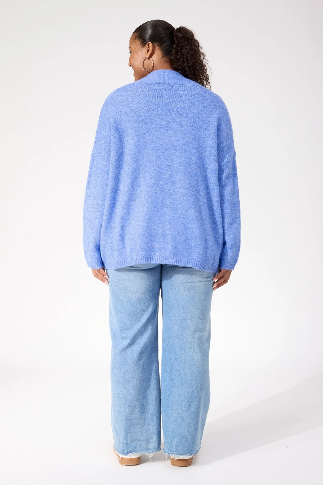 Image of Woman wearing Haven blue cardigan paired with denim jeans on a plain background