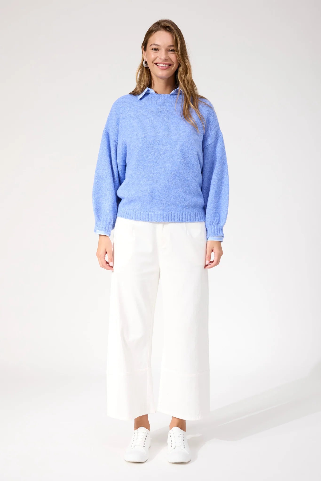 Image of Woman wearing blue Haven knit paired with white jeans and sneakers on a plain background