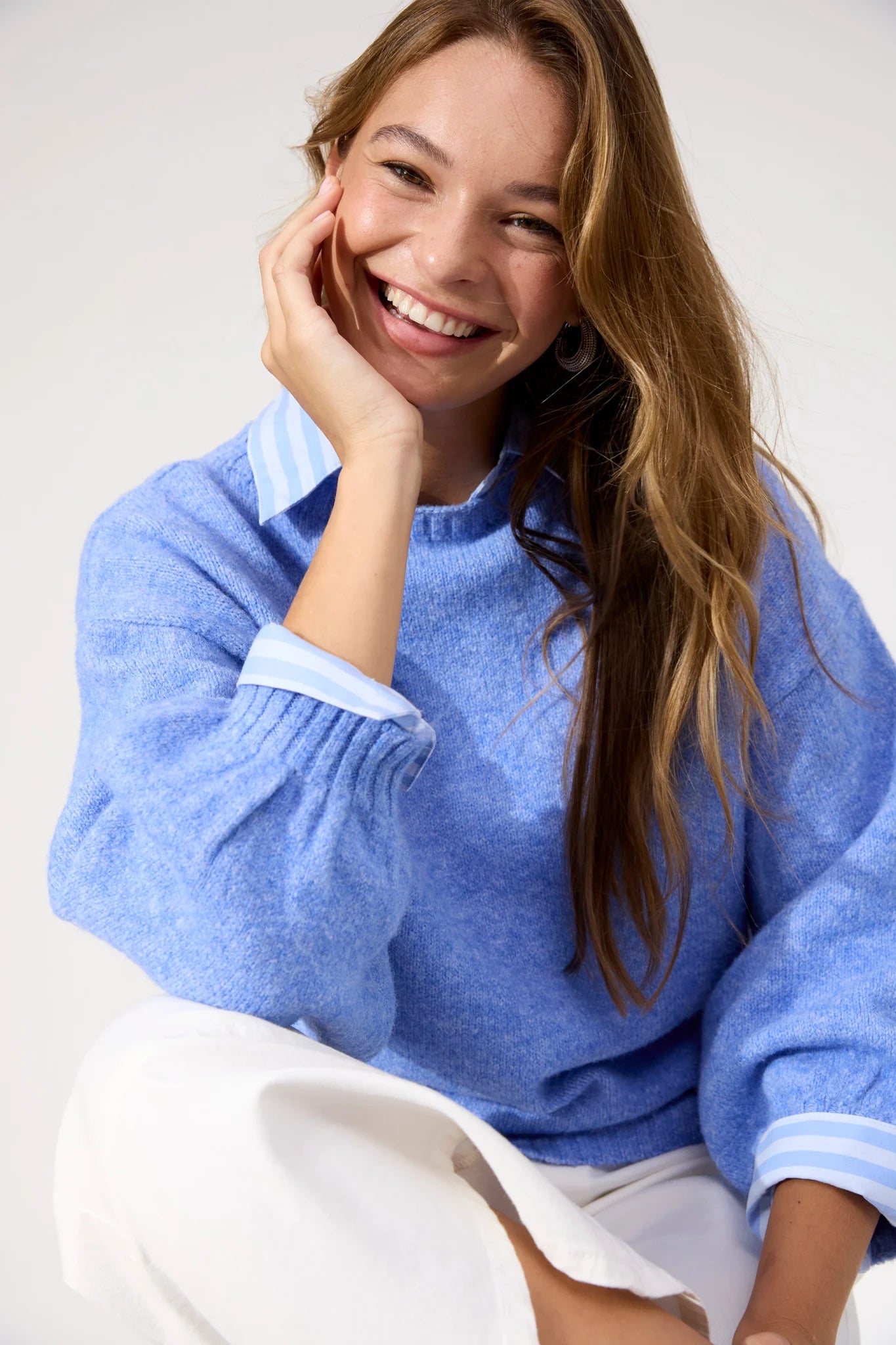 Woman wearing blue Haven knit paired with white jeans and sneakers on a plain background