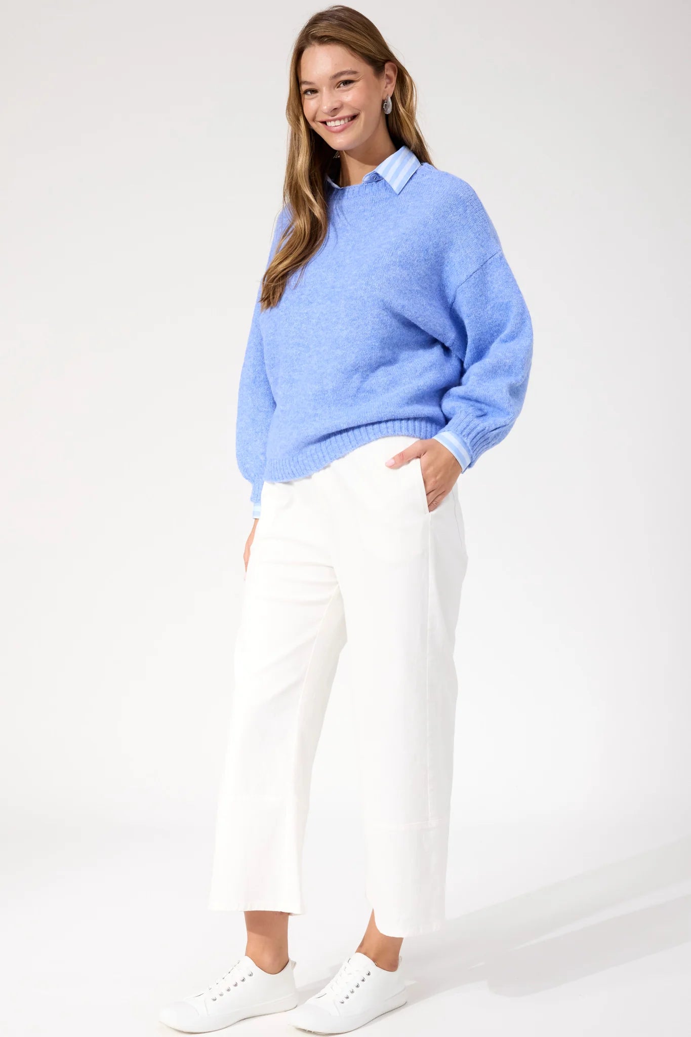 Image of Woman wearing blue Haven knit paired with white jeans and sneakers on a plain background