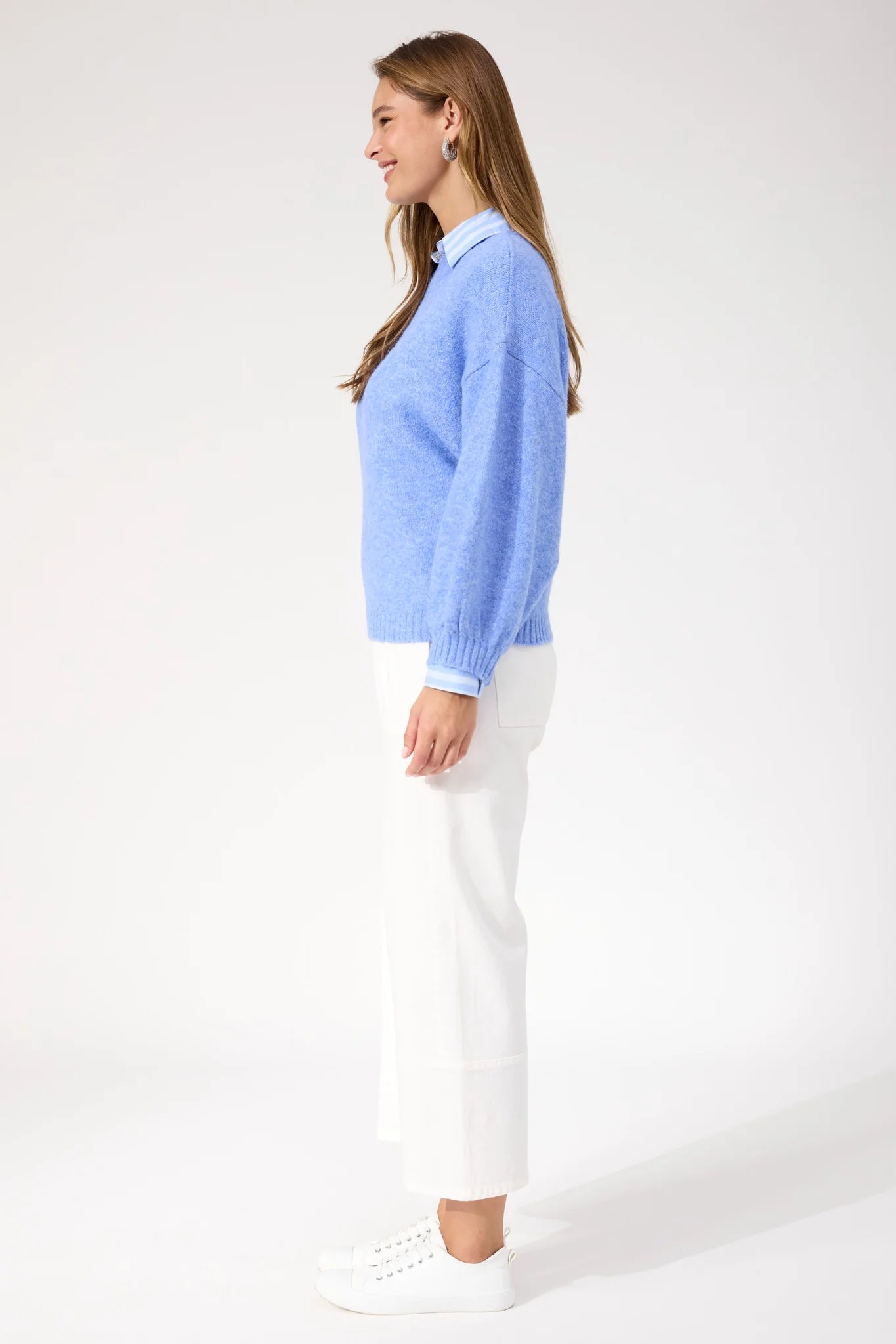 Woman wearing blue Haven knit paired with white jeans and sneakers on a plain background