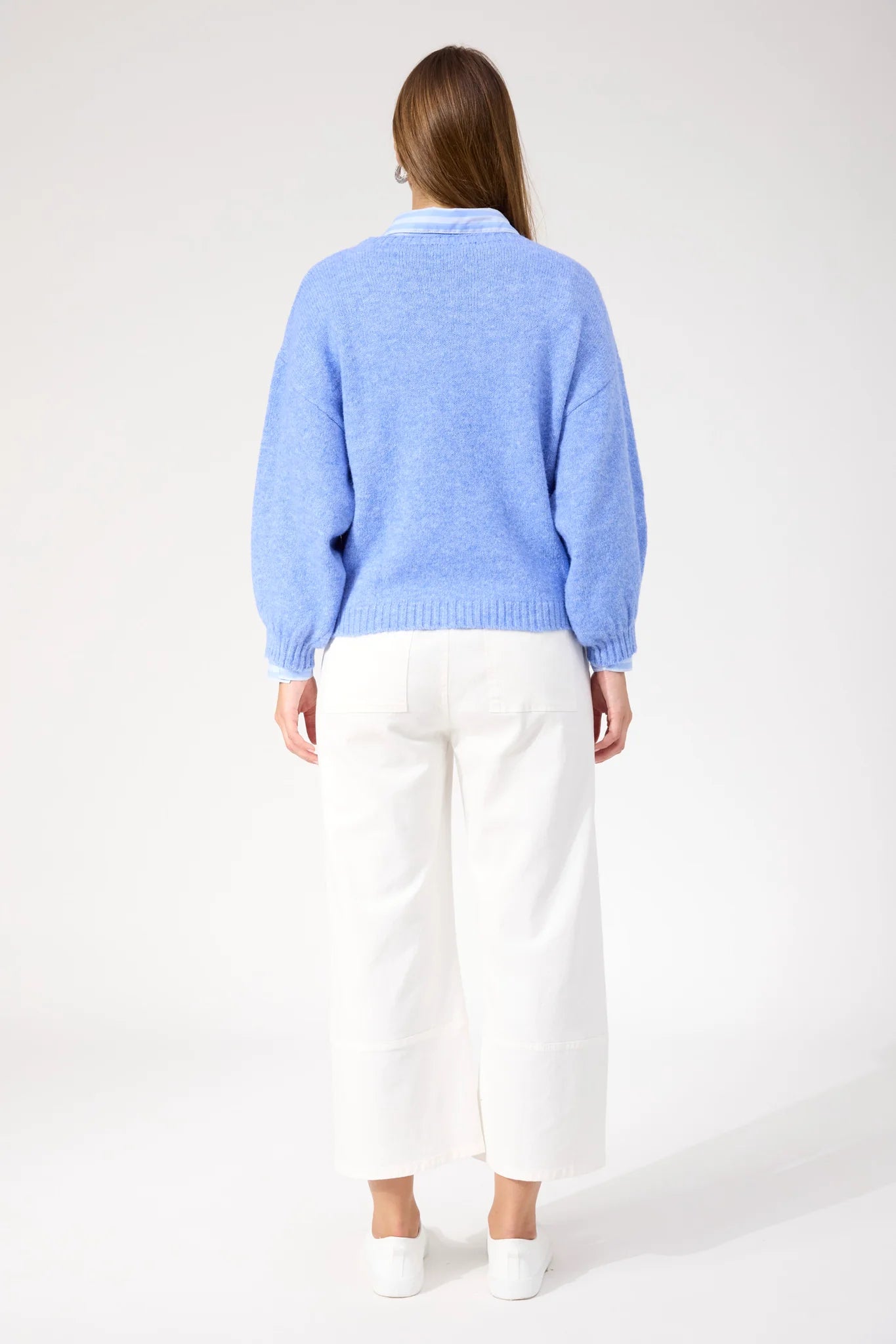Woman wearing blue Haven knit paired with white jeans and sneakers on a plain background