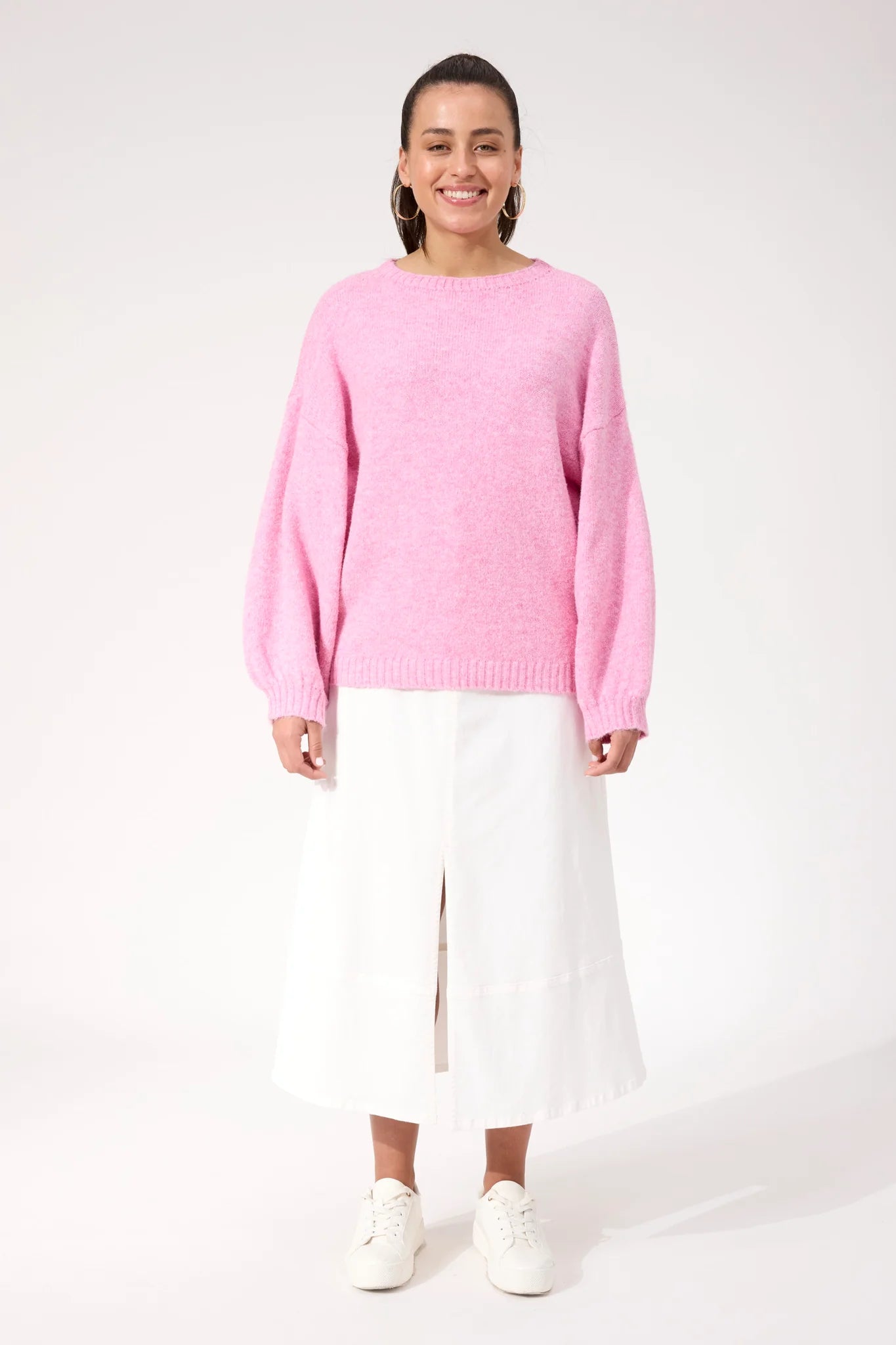 Image of Woman wearing a Haven pink knit paired with a white skirt on a plain background