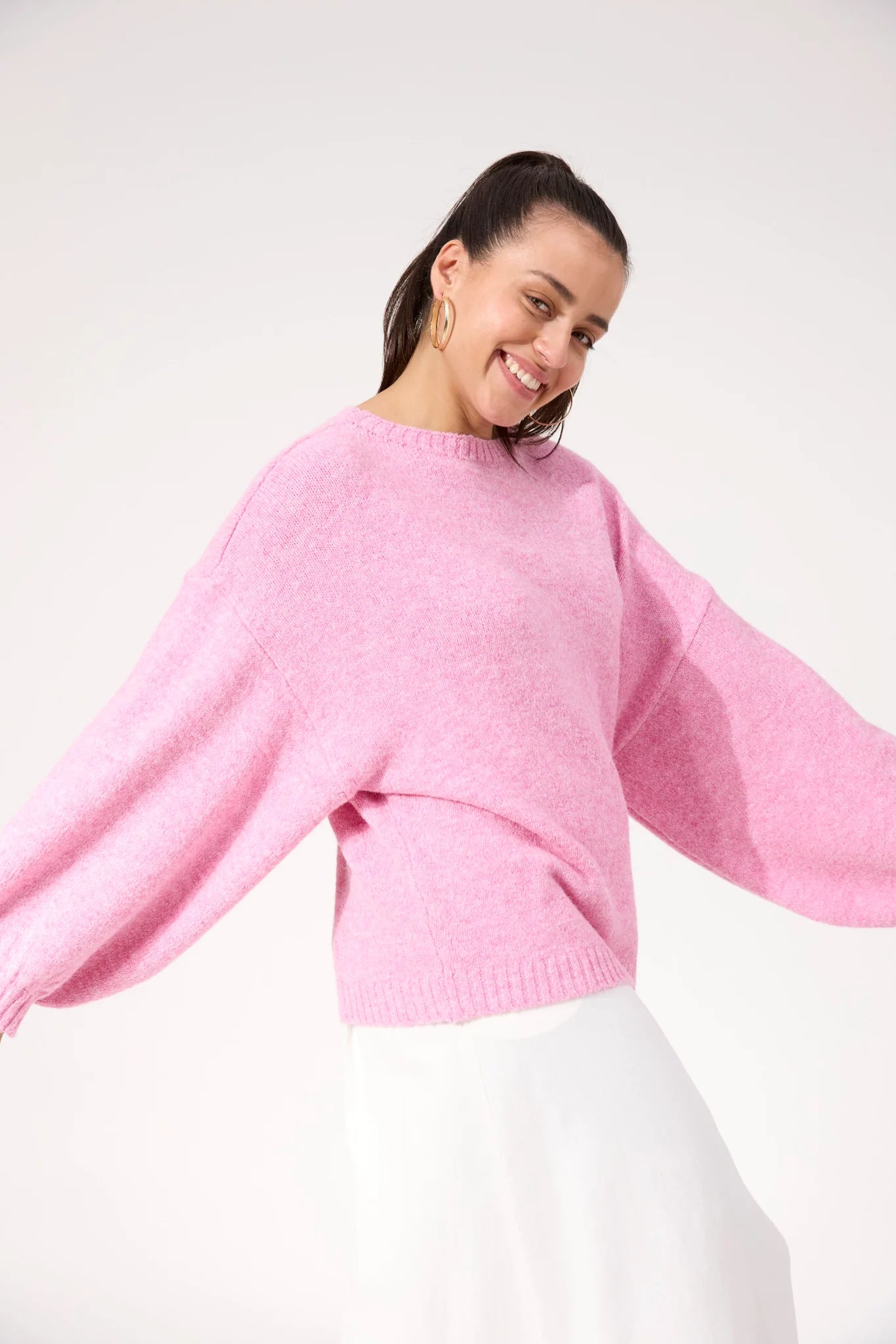Image of Woman wearing a Haven pink knit paired with a white skirt on a plain background