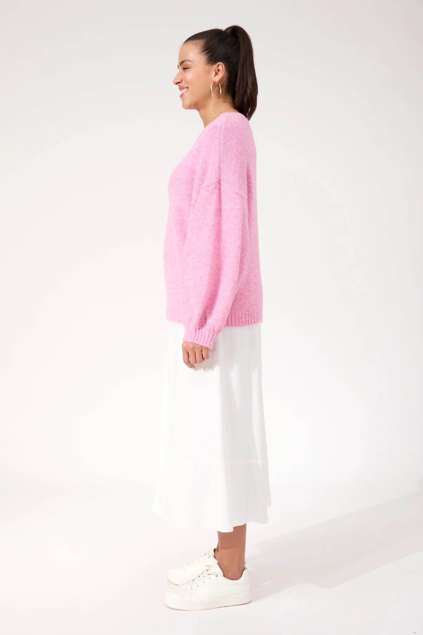 Image of Woman wearing a Haven pink knit paired with a white skirt on a plain background