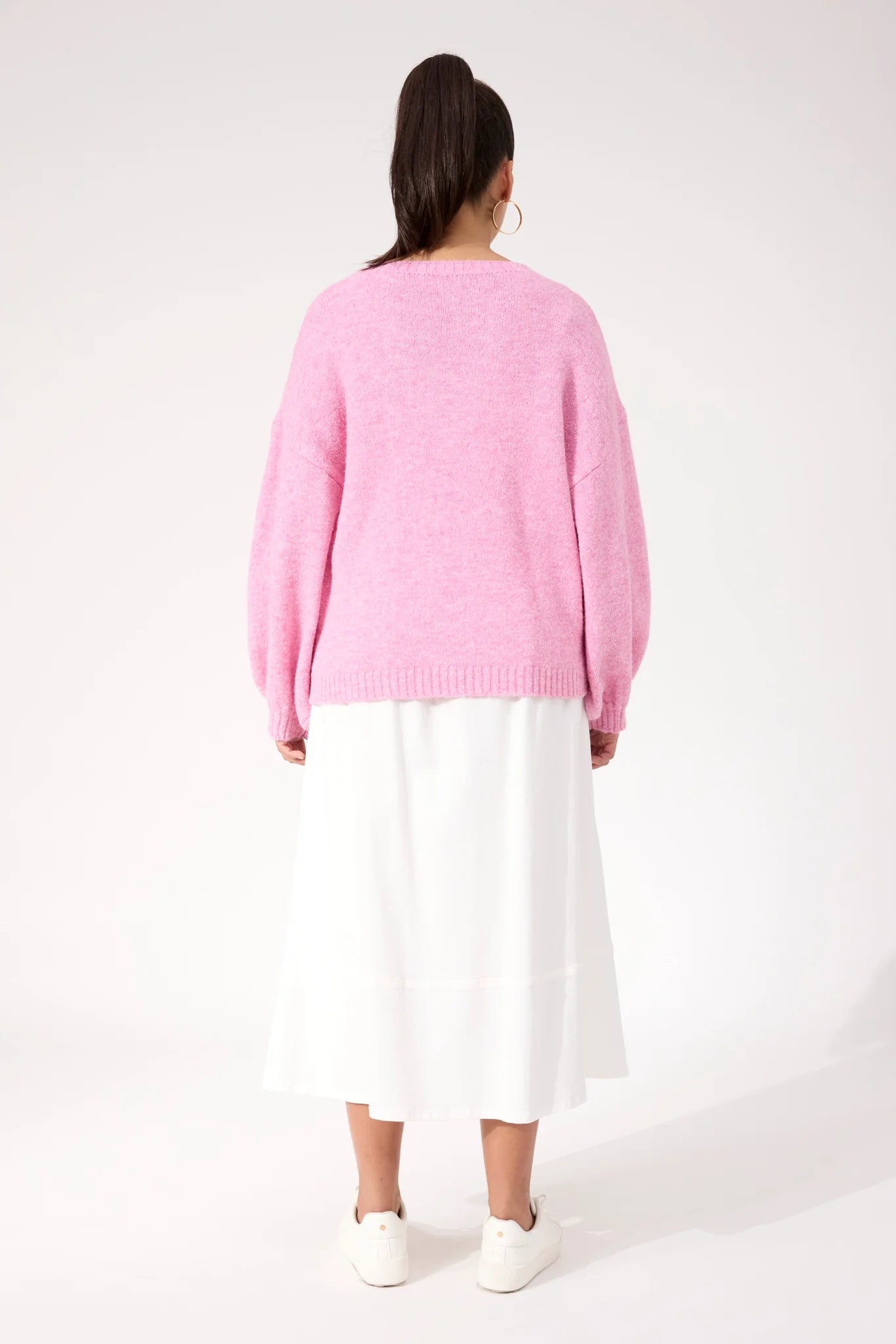 Woman wearing a Haven pink knit paired with a white skirt on a plain background