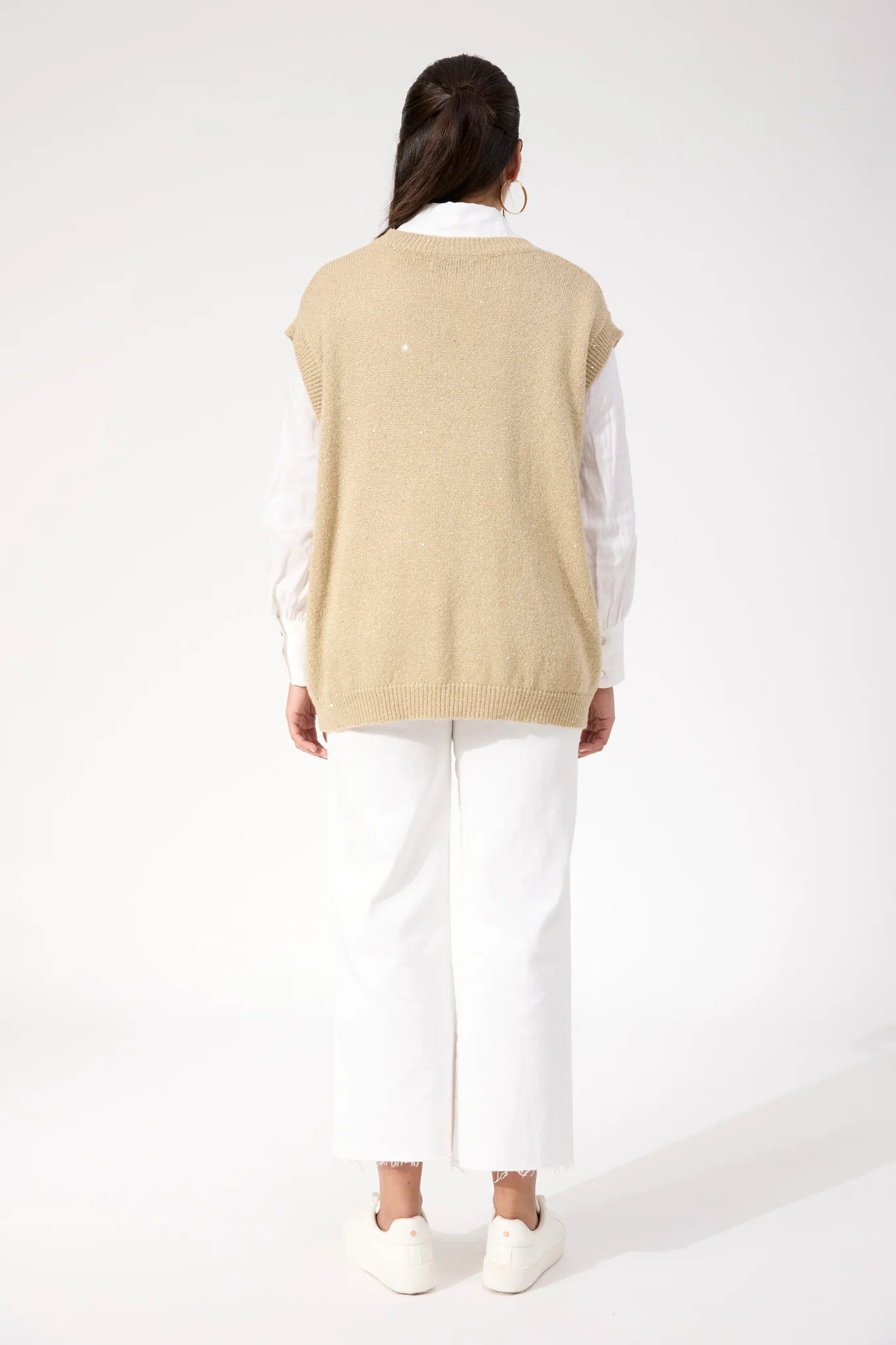 Image of Woman wearing Haven sparkle vest paired with white jeans on a plain background