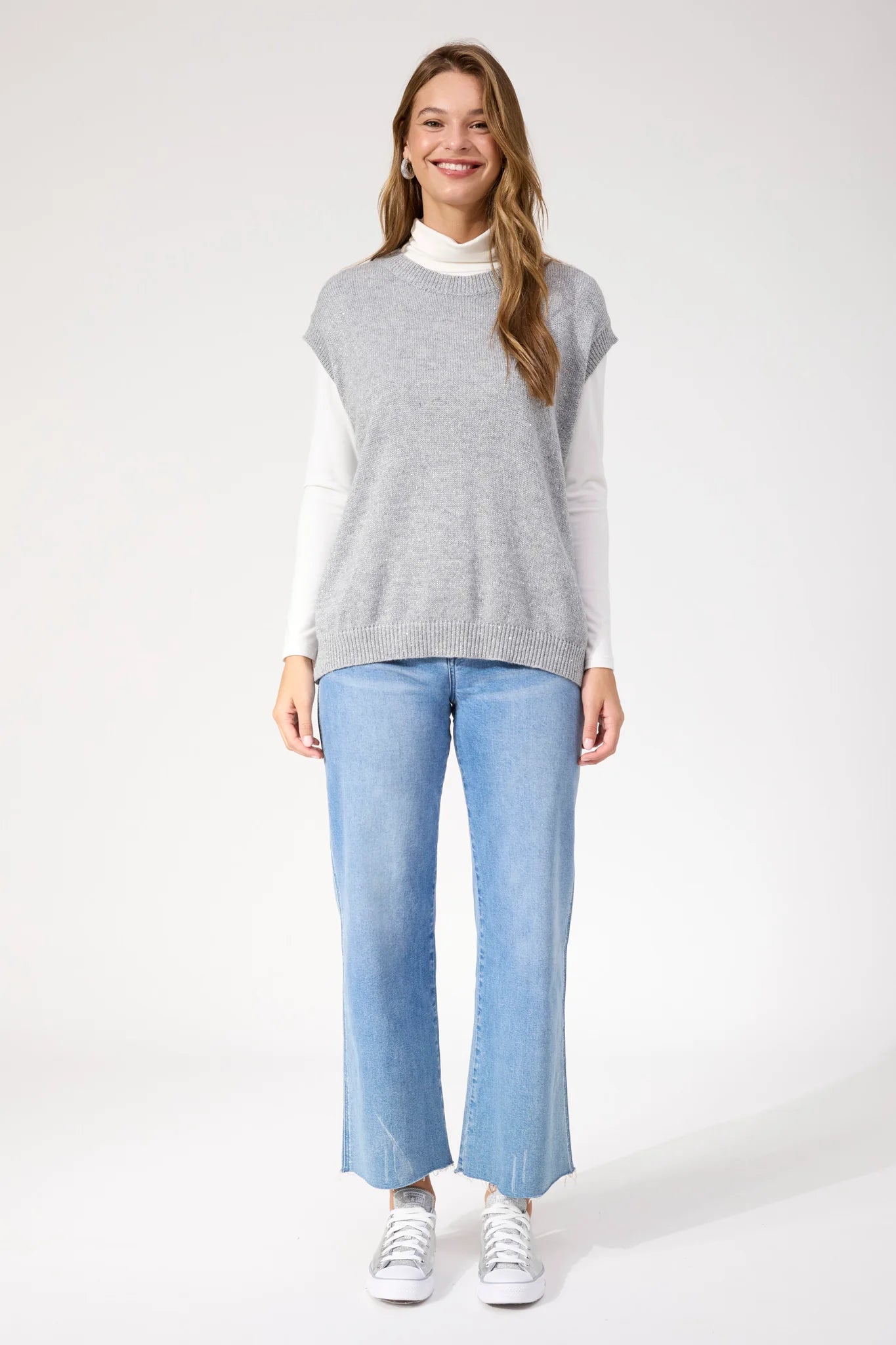 Image of Woman wearing Haven silver vest paired with denim jeans on a white background