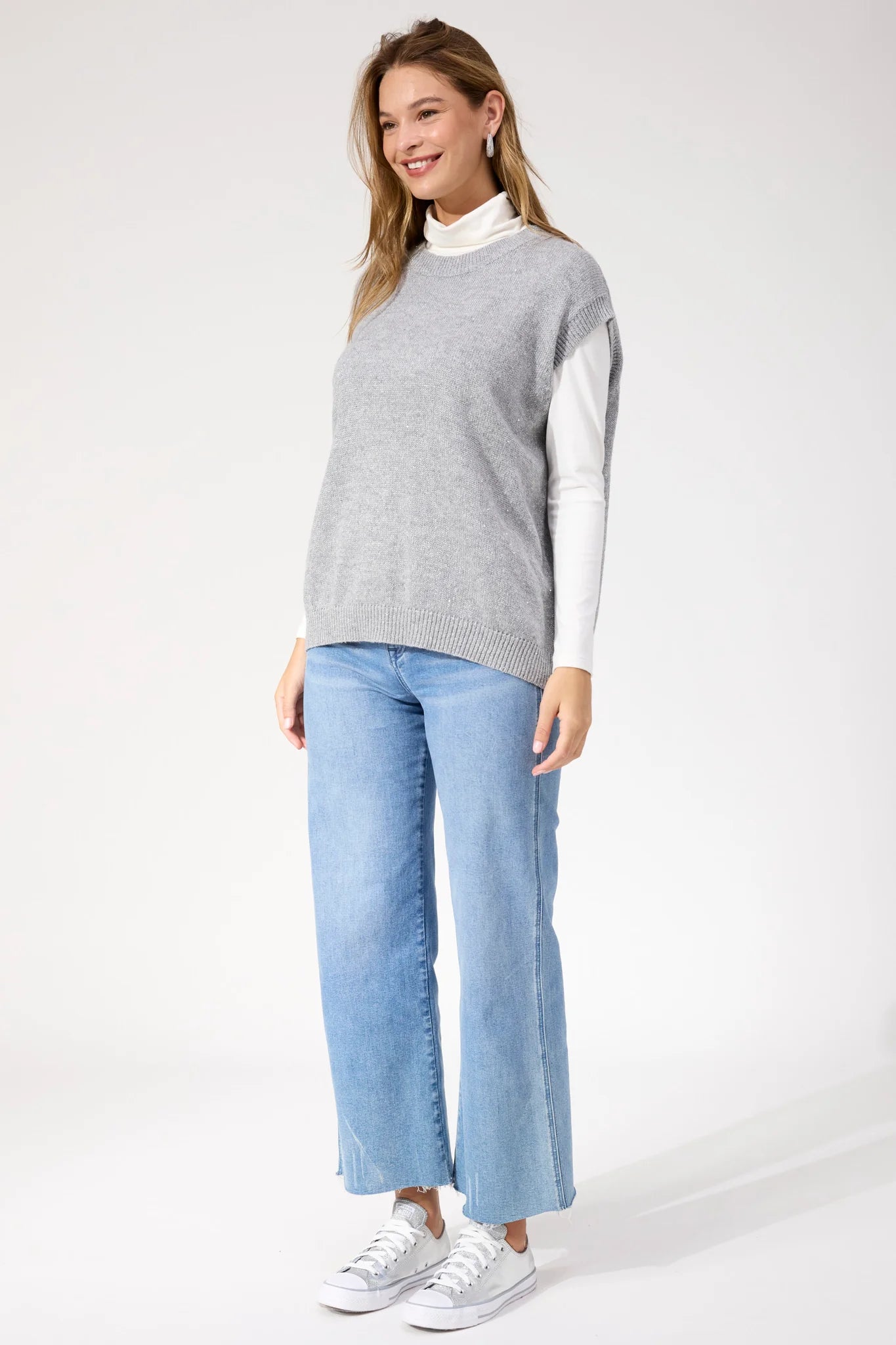 Image of Woman wearing Haven silver vest paired with denim jeans on a white background