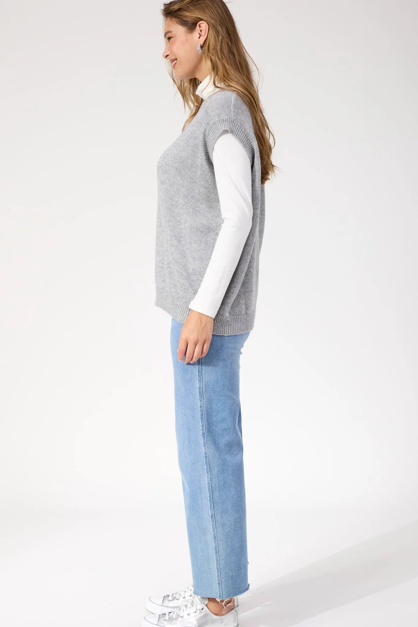 Image of Woman wearing Haven silver vest paired with denim jeans on a white background