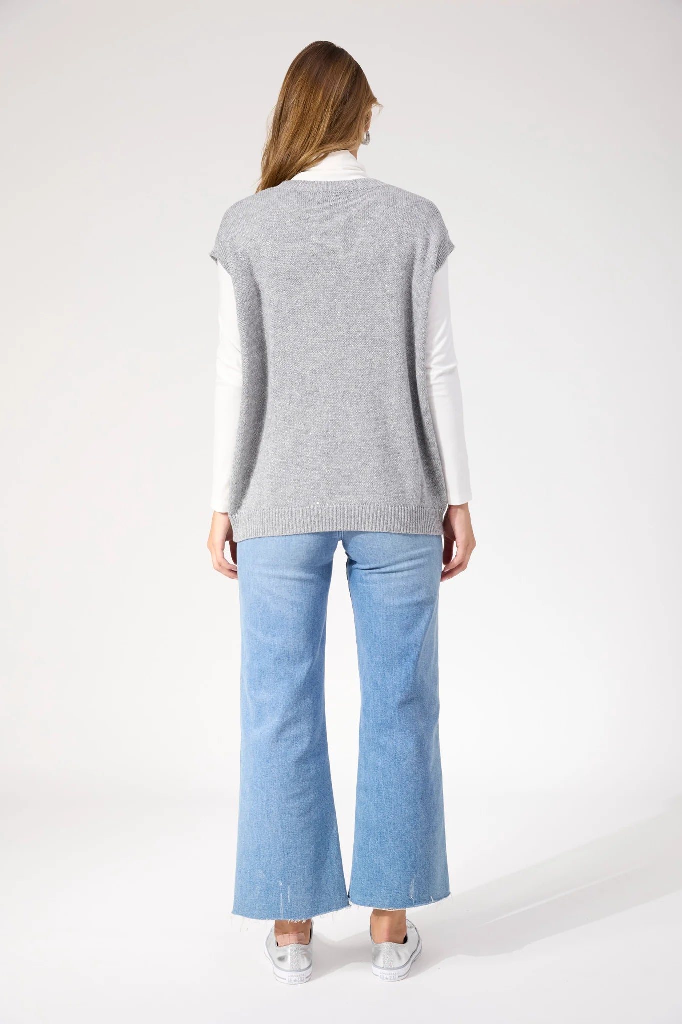 Image of Woman wearing Haven silver vest paired with denim jeans on a white background