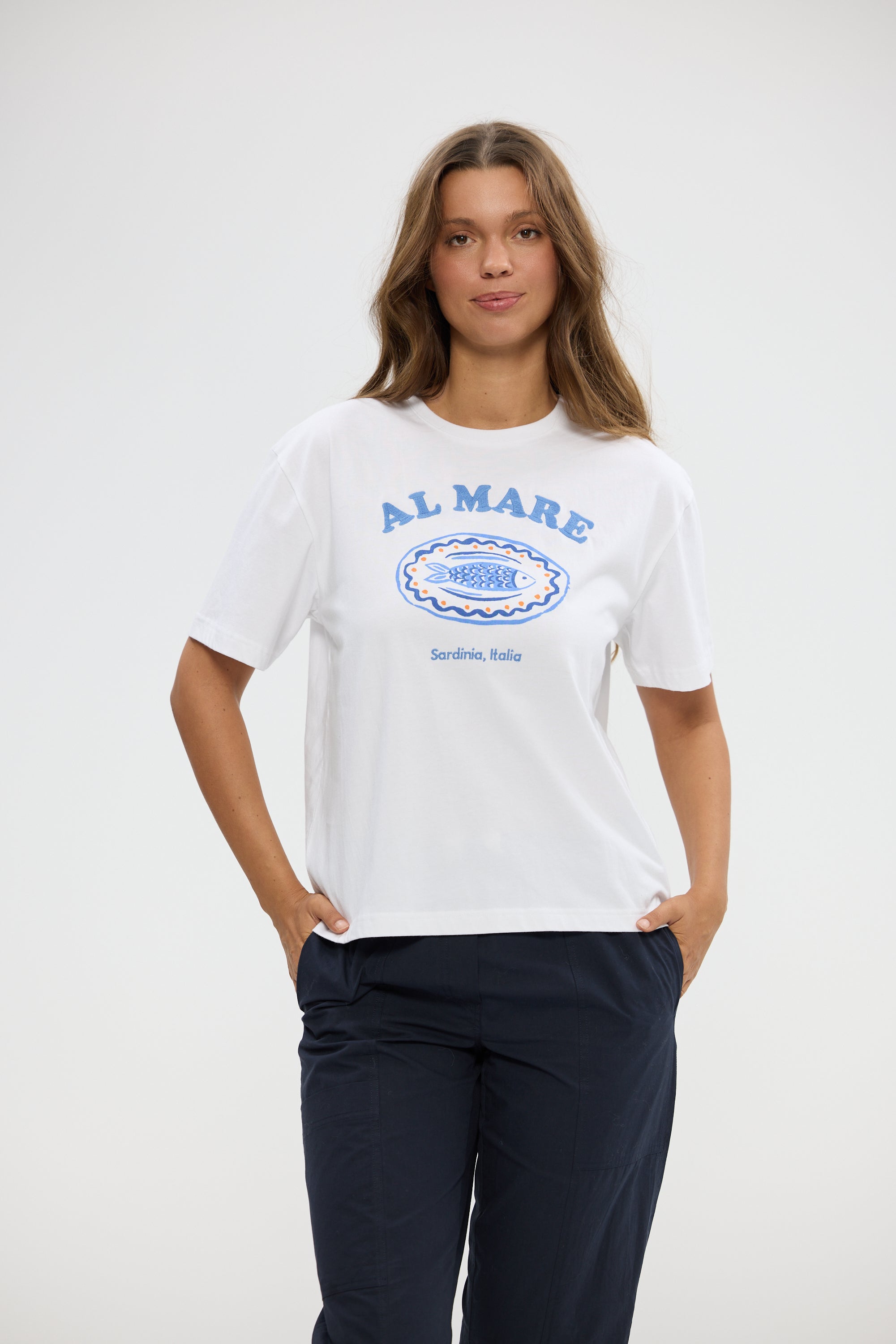 Image of Woman wearing a Holiday white t-shirt with 'Al Mare' text and navy pants on a white background