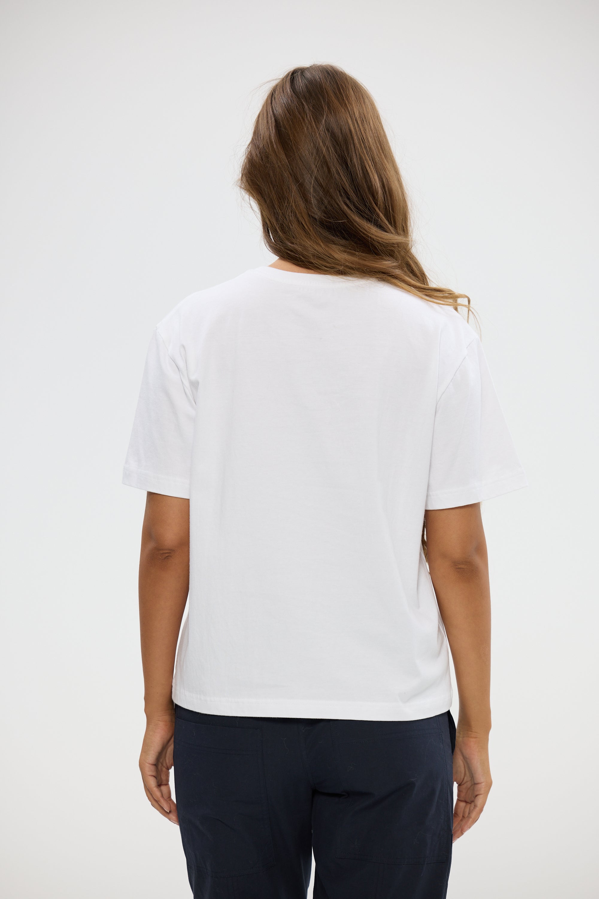 Image of Woman wearing a Holiday white t-shirt and dark pants on a plain background