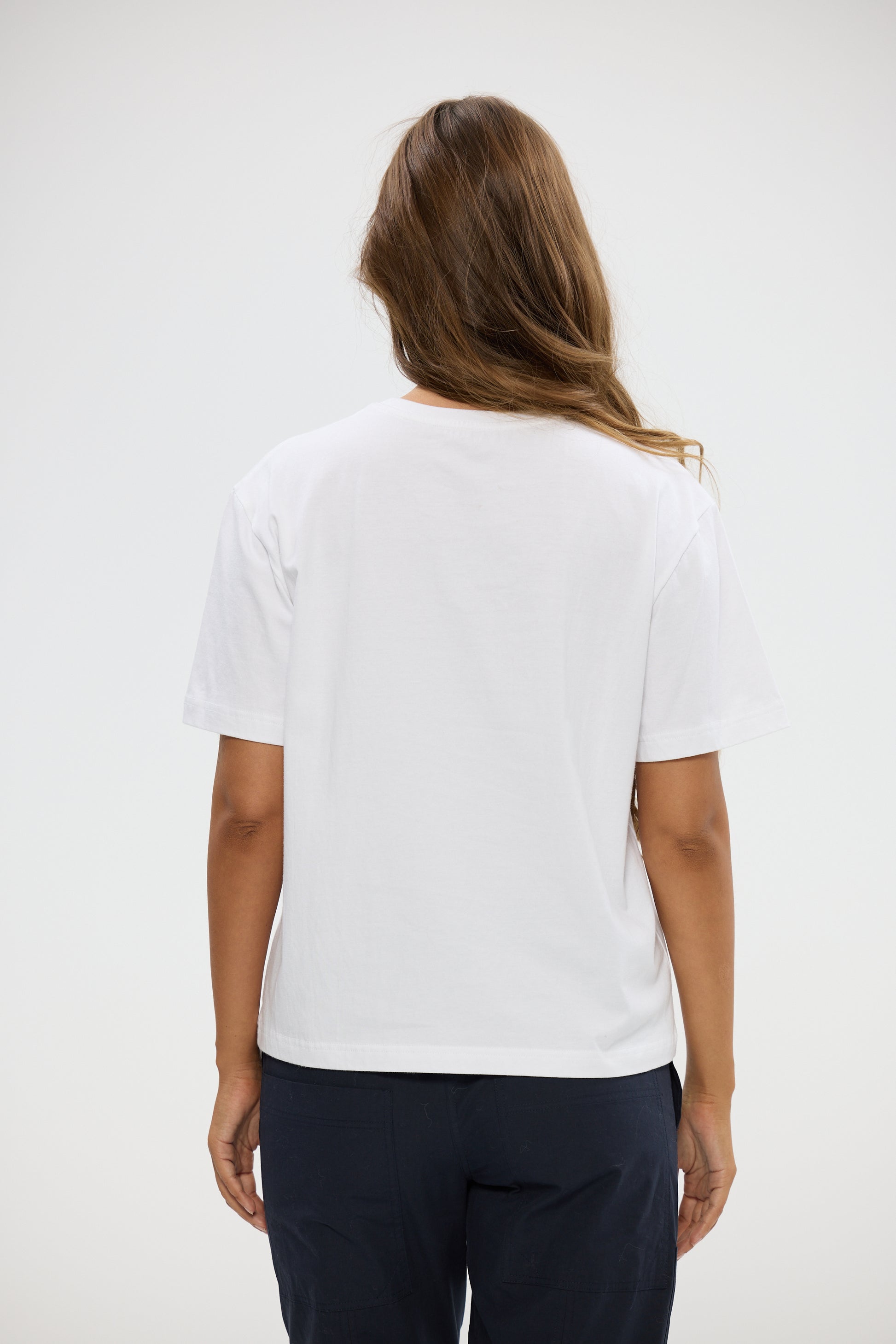 Woman wearing a Holiday white t-shirt and dark pants on a plain background