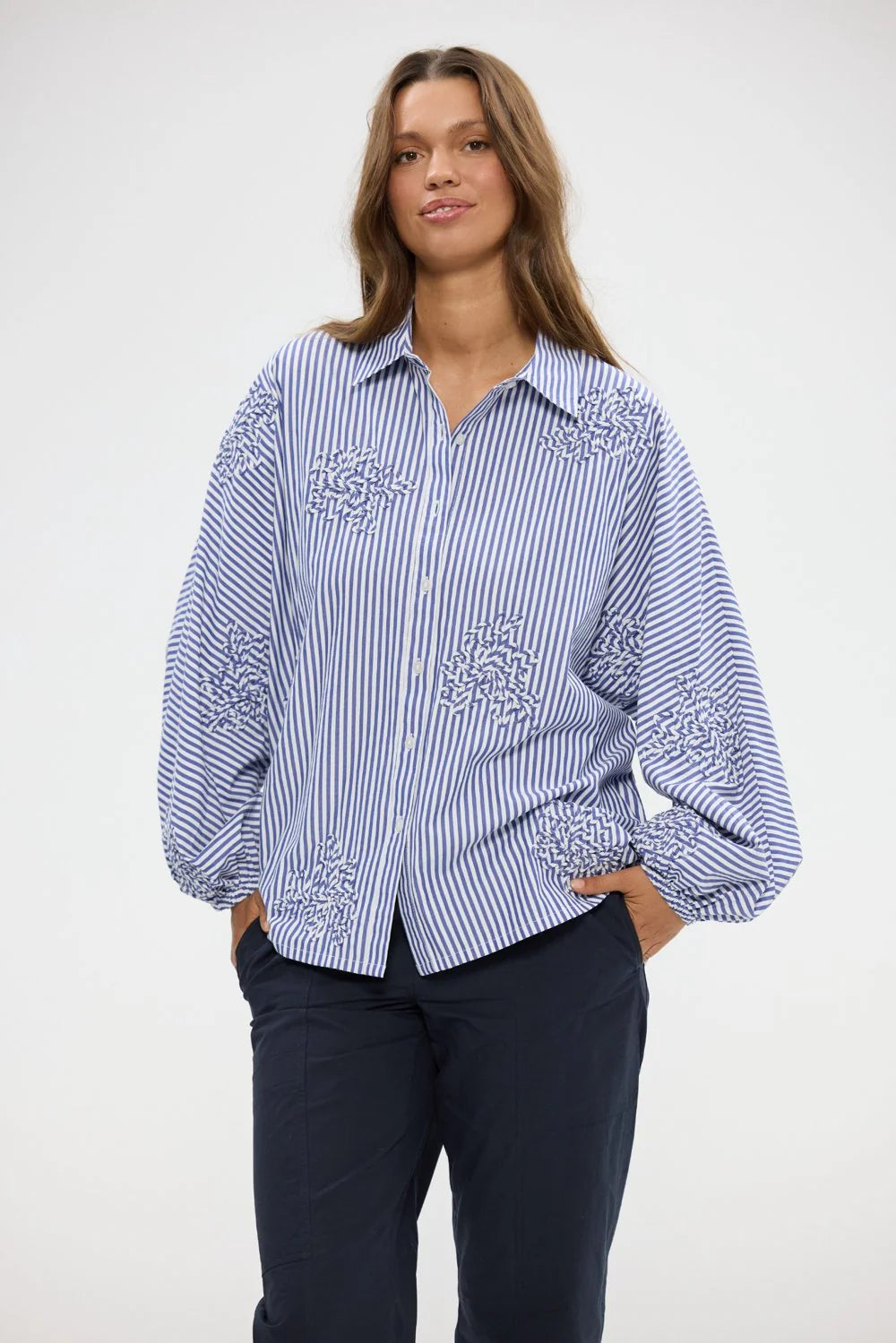 Woman wearing a Holiday blue and white striped shirt with floral embroidery on a white background