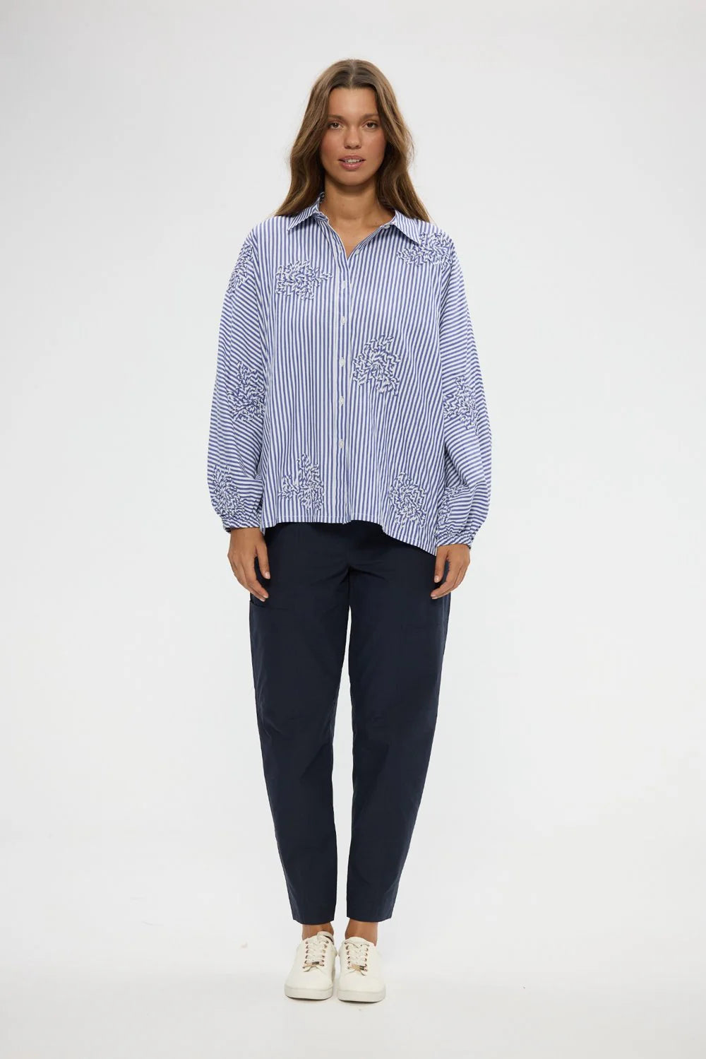 Image of Woman wearing a Holiday blue and white striped shirt with embroidery, paired with navy pants on a white background