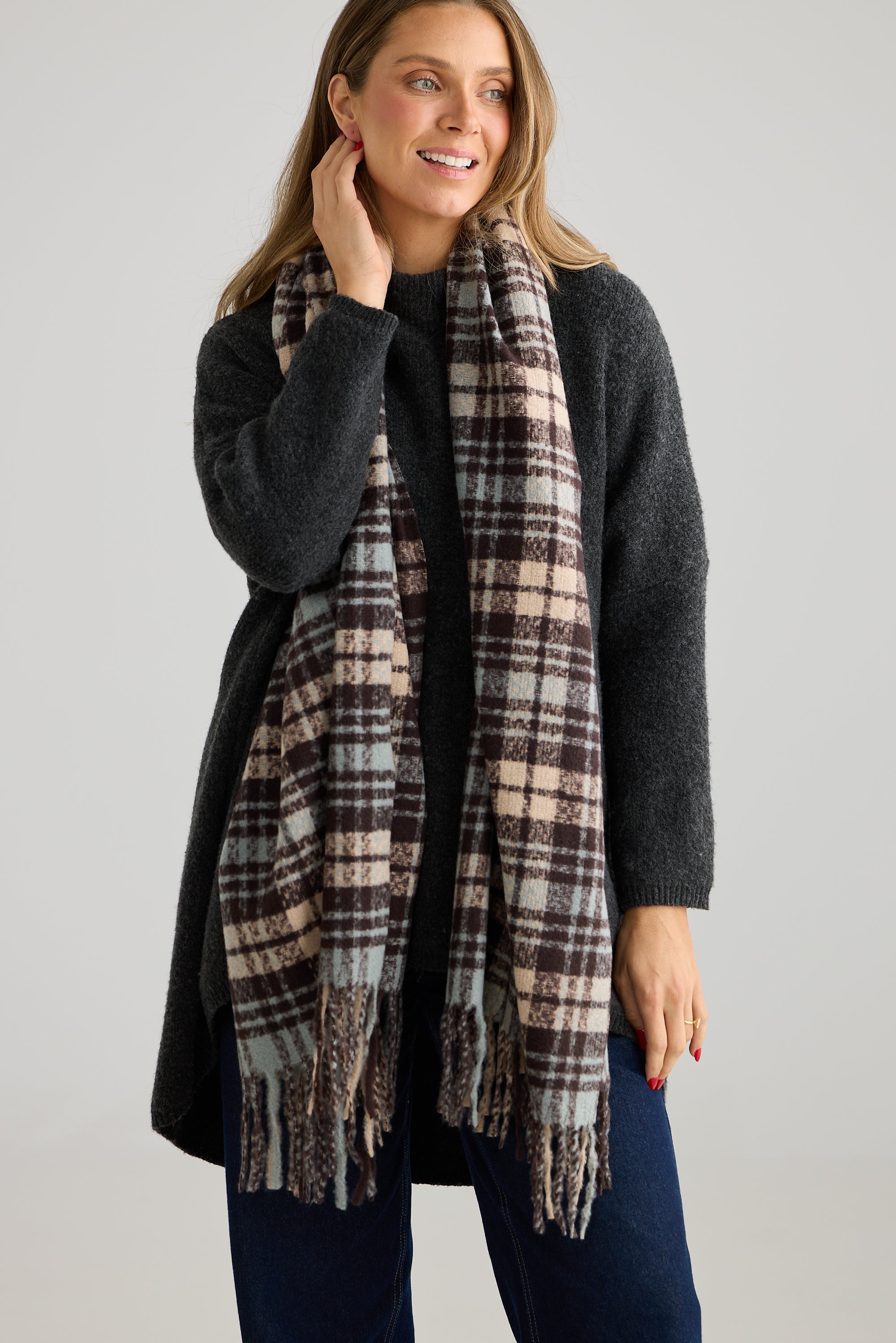 Image of Woman wearing a Holiday Life plaid scarf and dark coat on a plain background