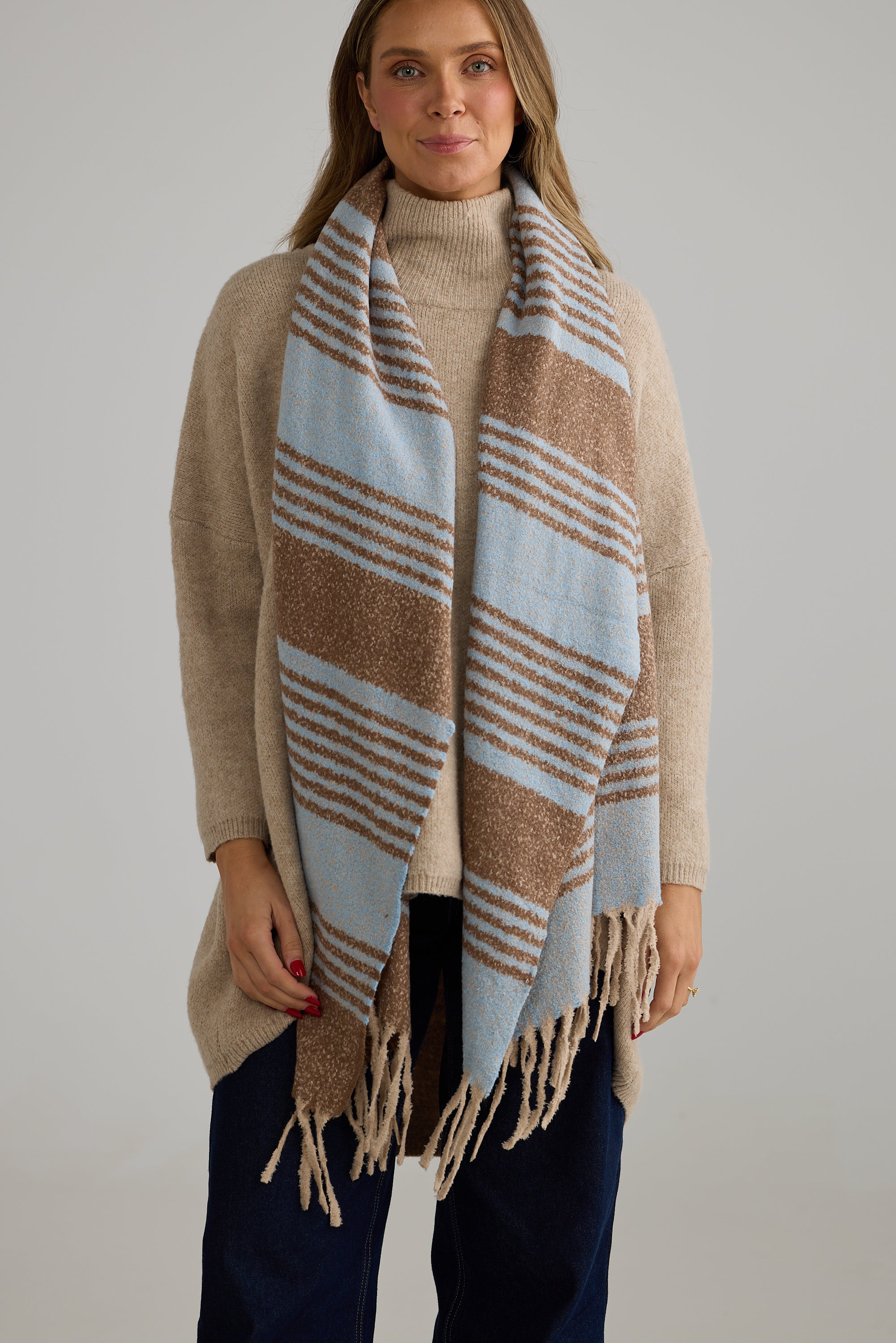Image of Woman wearing a Holiday Life beige and blue striped scarf against a plain background