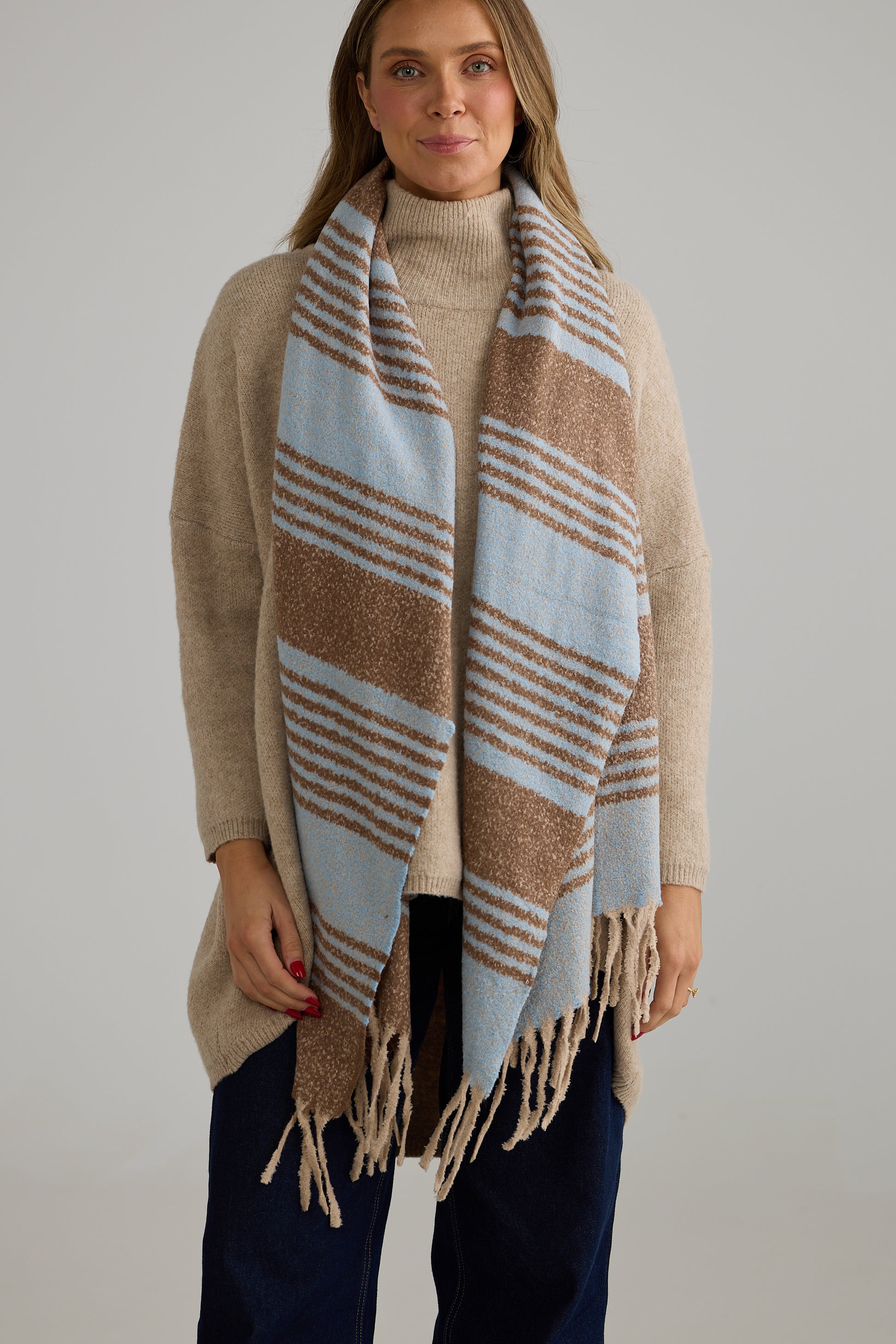 Woman wearing a Holiday Life beige and blue striped scarf against a plain background
