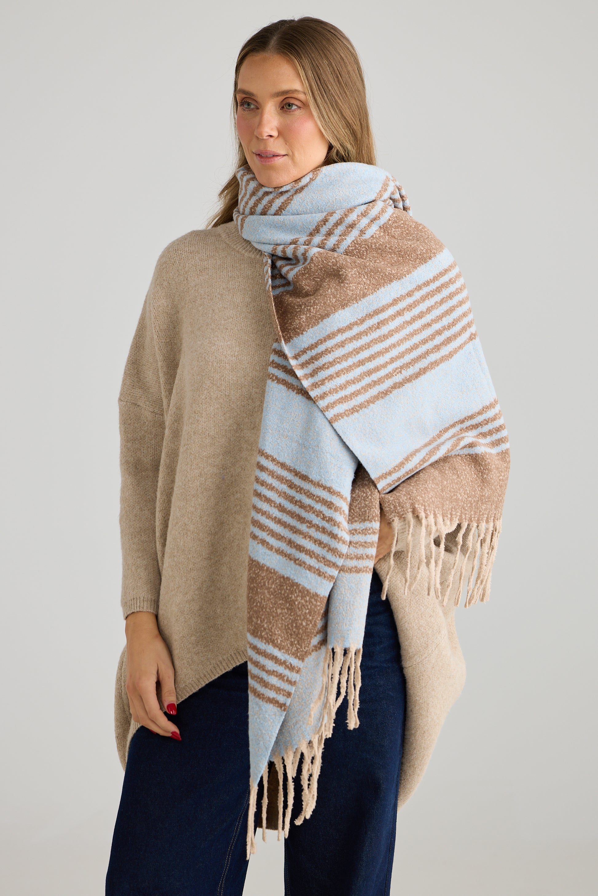 Woman wearing a Holiday Life beige and blue striped scarf on a plain background