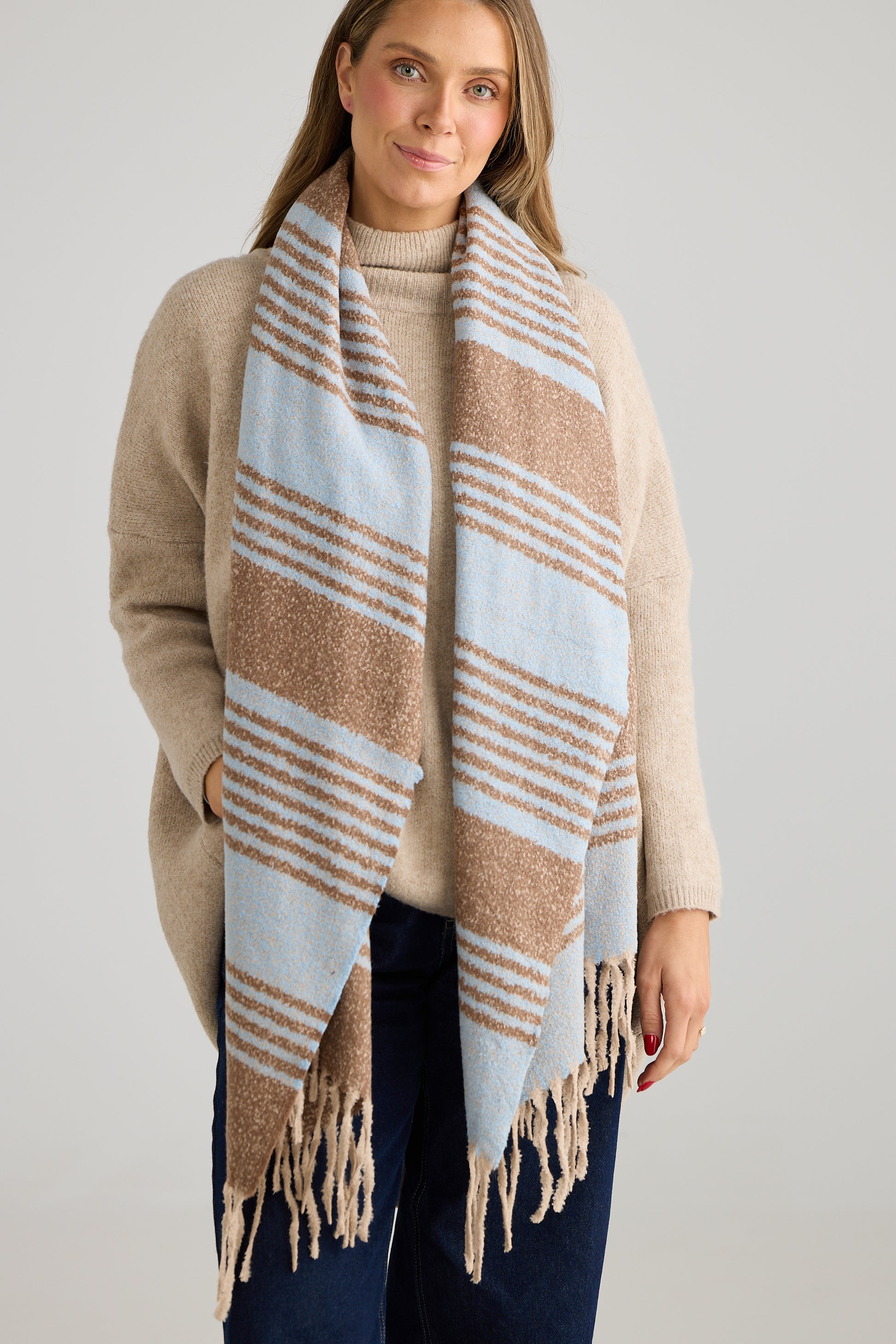 Woman wearing a Holiday Life beige and blue striped scarf on a plain background
