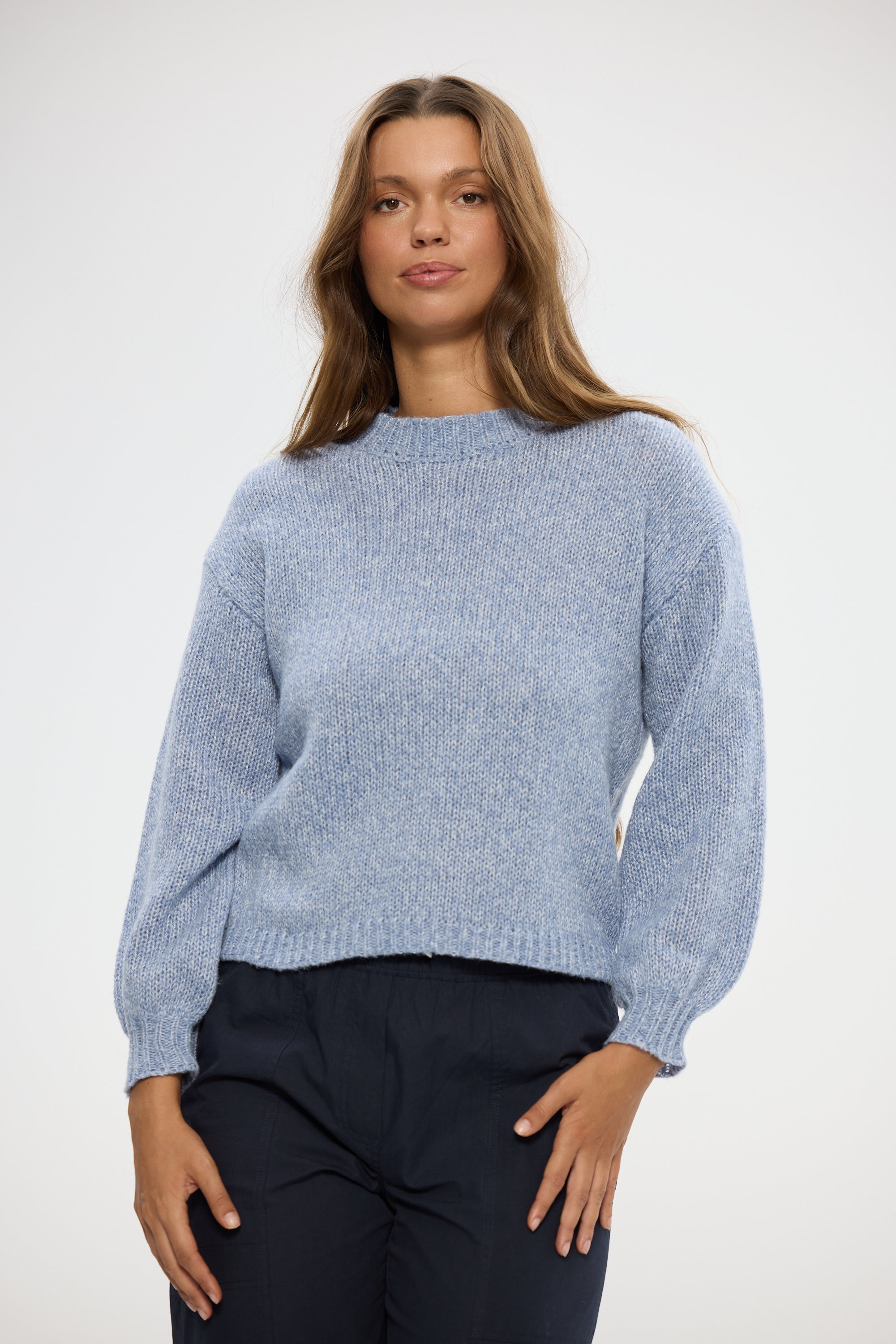 Image of Woman wearing a Holiday light blue sweater and dark pants on a white background
