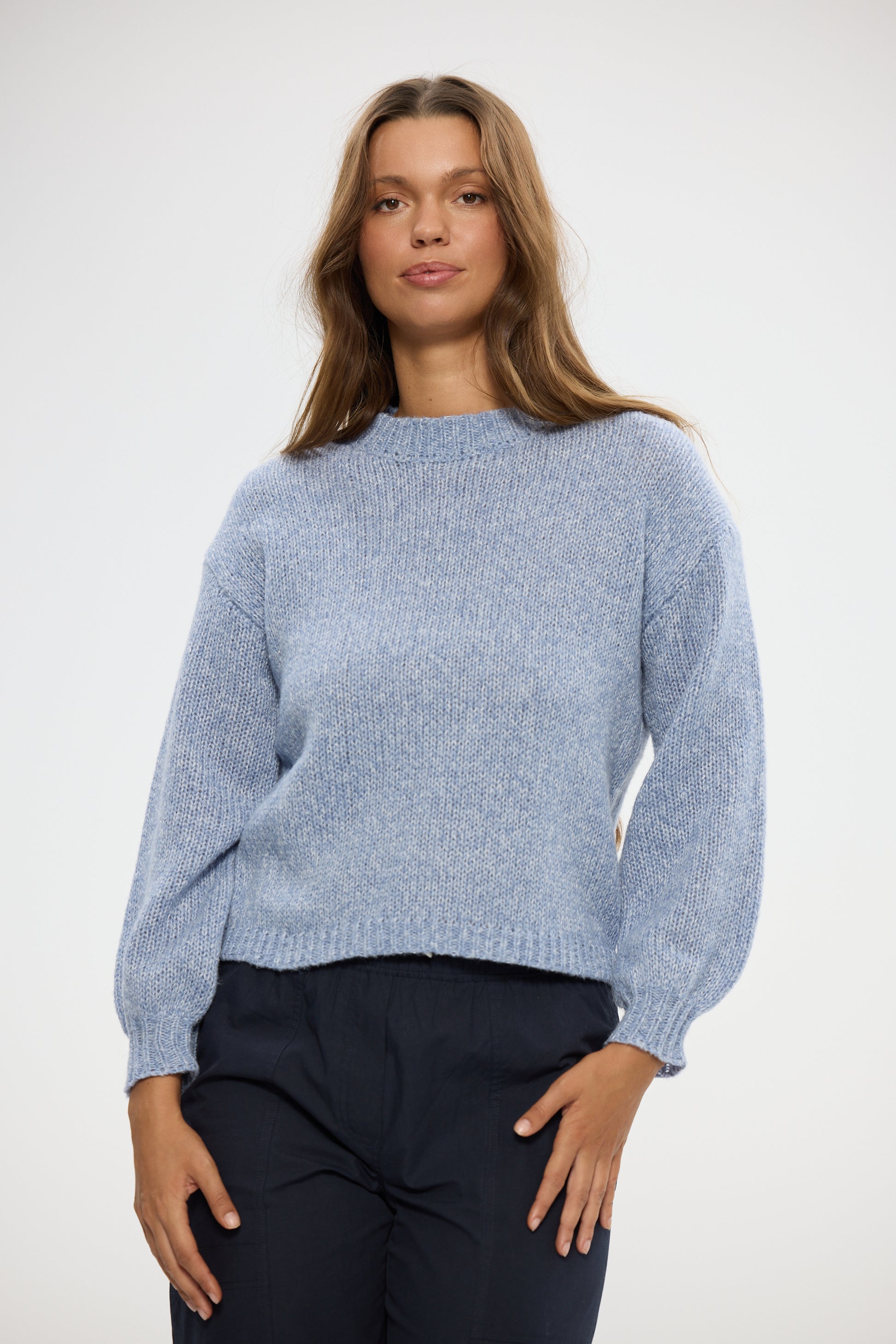 Woman wearing a Holiday light blue sweater and dark pants on a white background