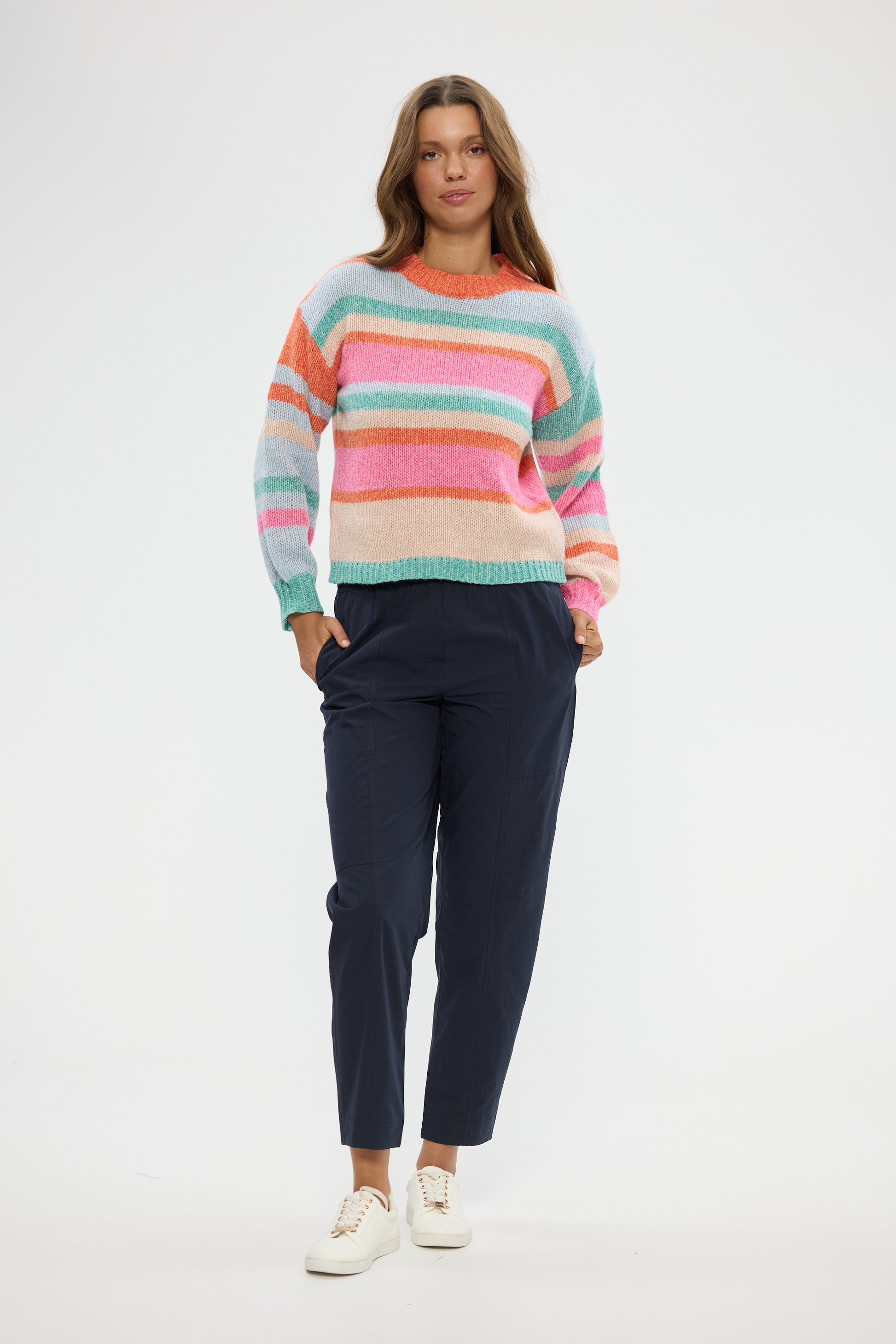 Woman wearing a Holiday colorful striped sweater and navy pants on a white background