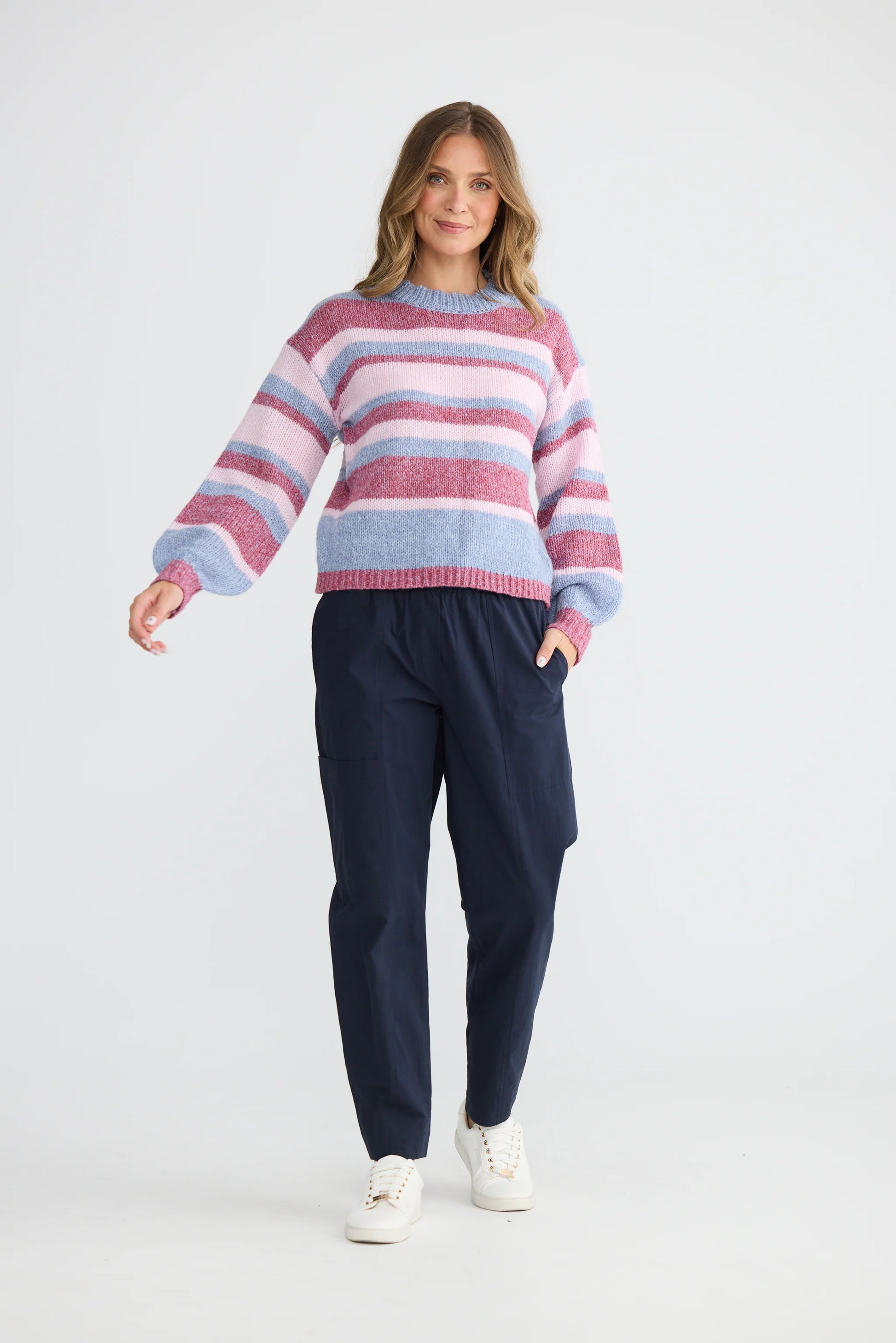 Woman wearing a Holiday striped sweater and navy pants on a white background