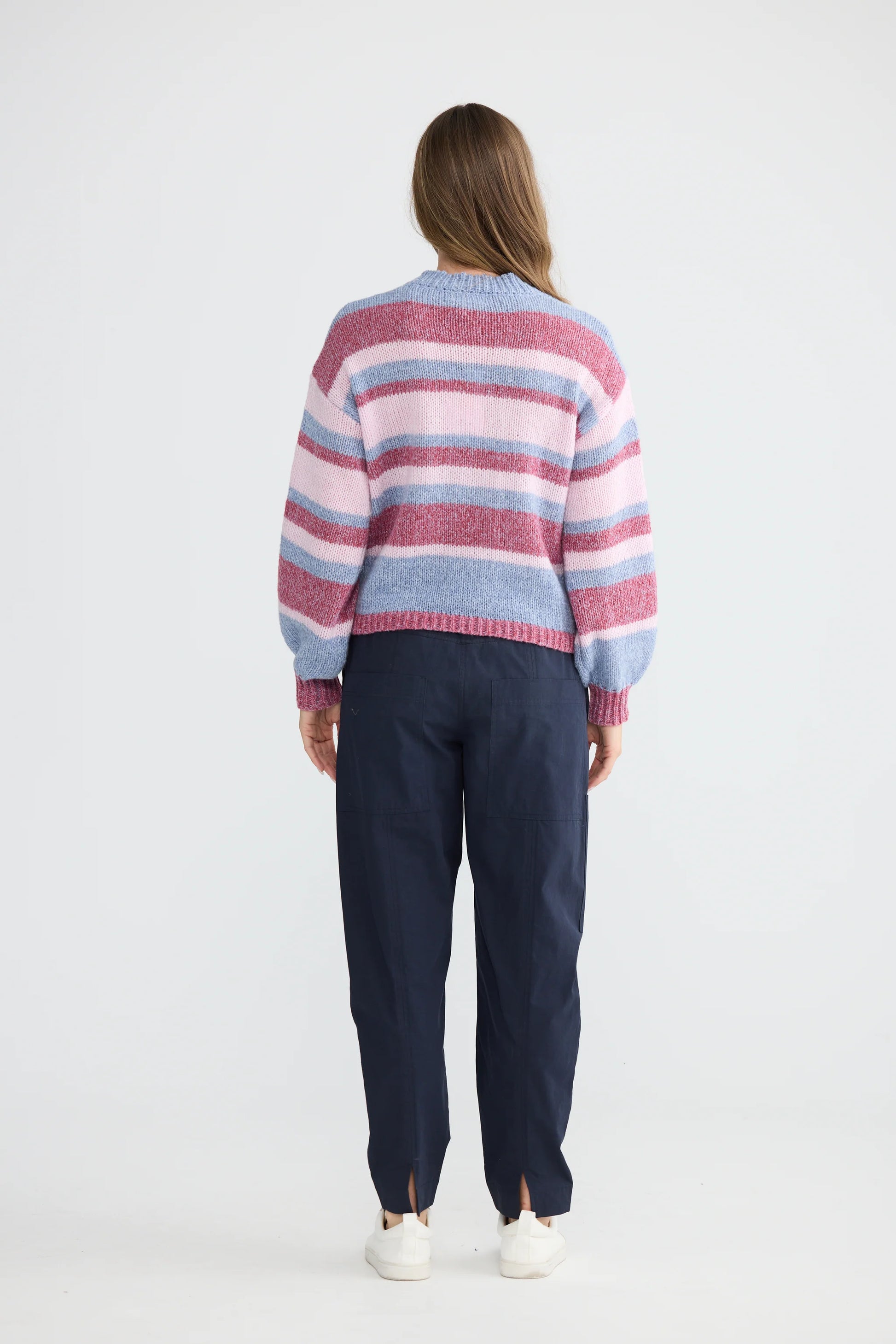 Woman wearing a Holiday striped sweater and dark pants on a white background