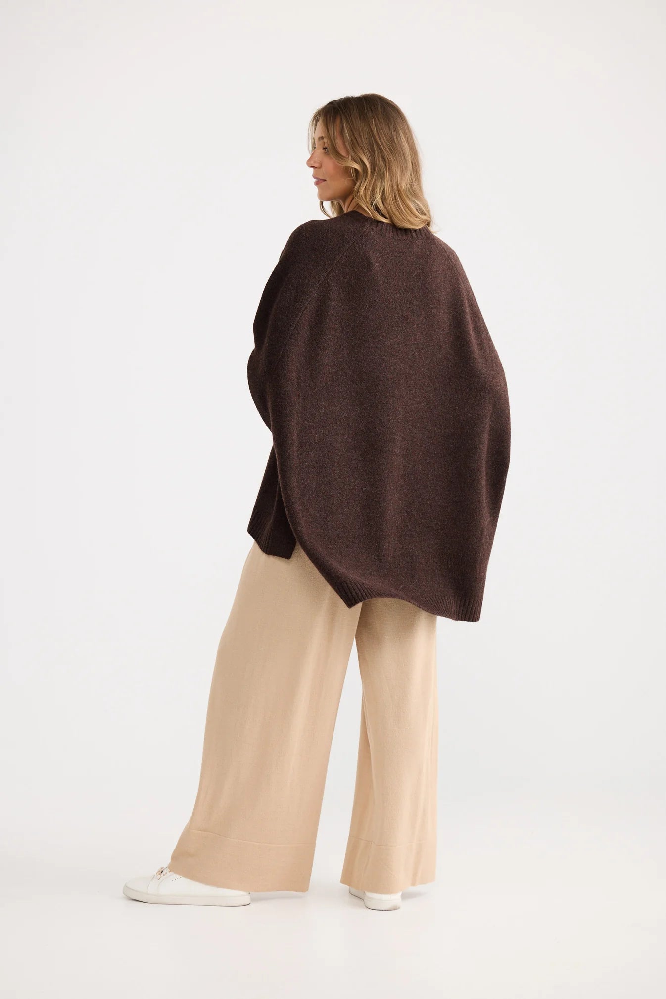 Woman wearing a Home Love brown poncho and beige pants on a white background